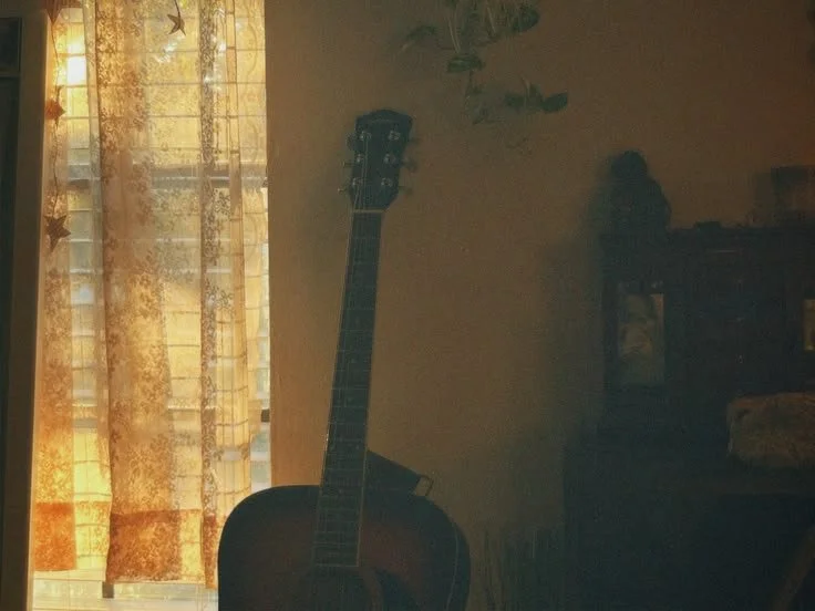 a dusty guitar sits in a room by a curtained window