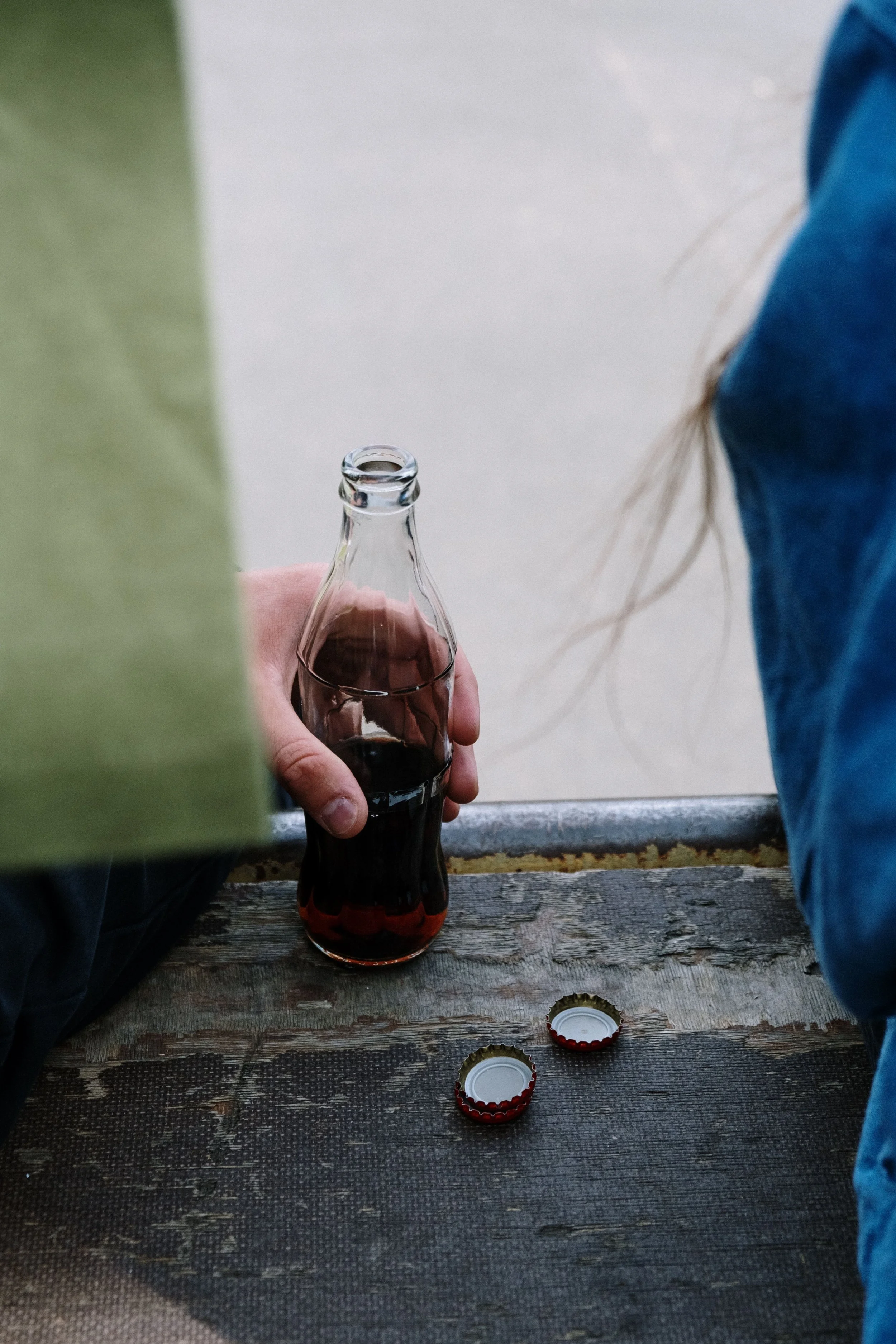 A relaxed scene with a glass soda bottle and bottle caps overlooking an outdoor view..