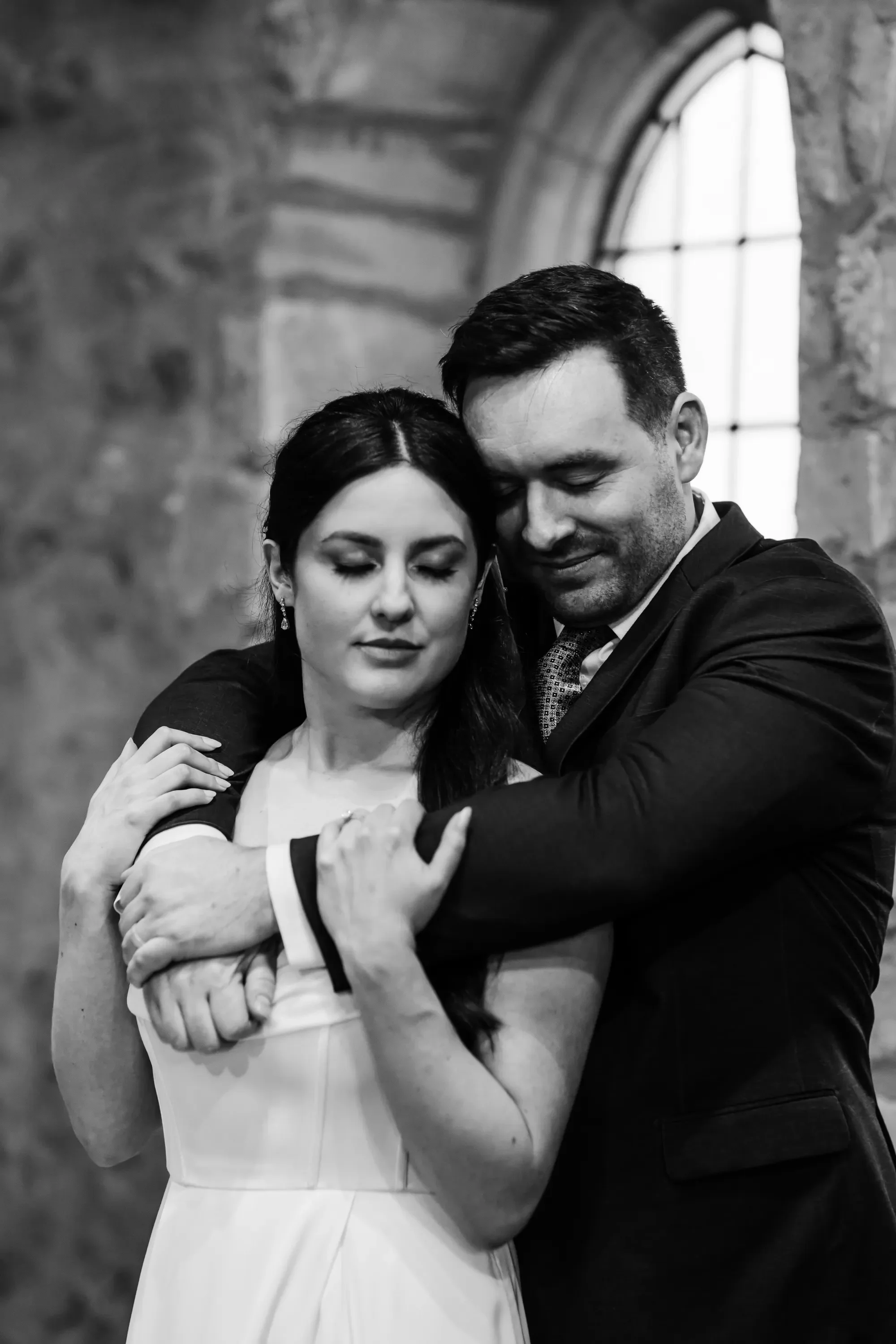 21-post-ceremony-embrace-by-window-bw-pilgrim-chapel-kansas-city.webp
