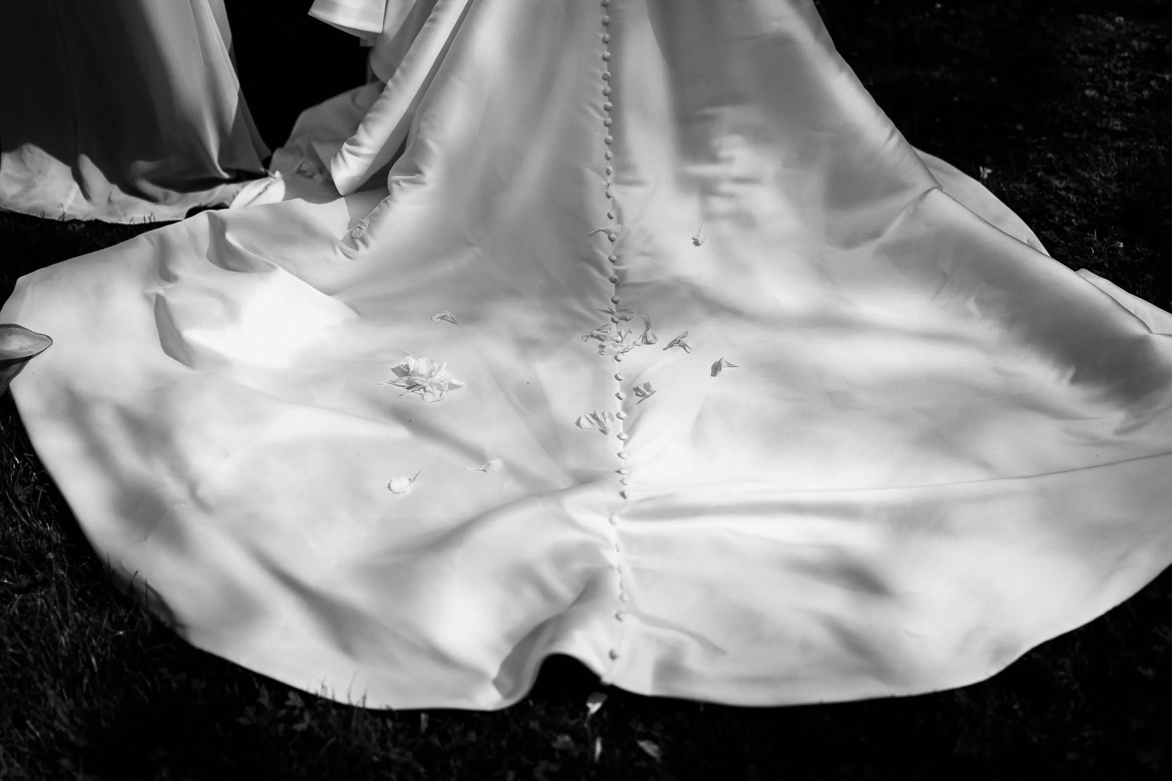 A close-up of a white wedding dress train with buttons, scattered rose petals, and shadows—captured by a Grosse Ile wedding photographer.