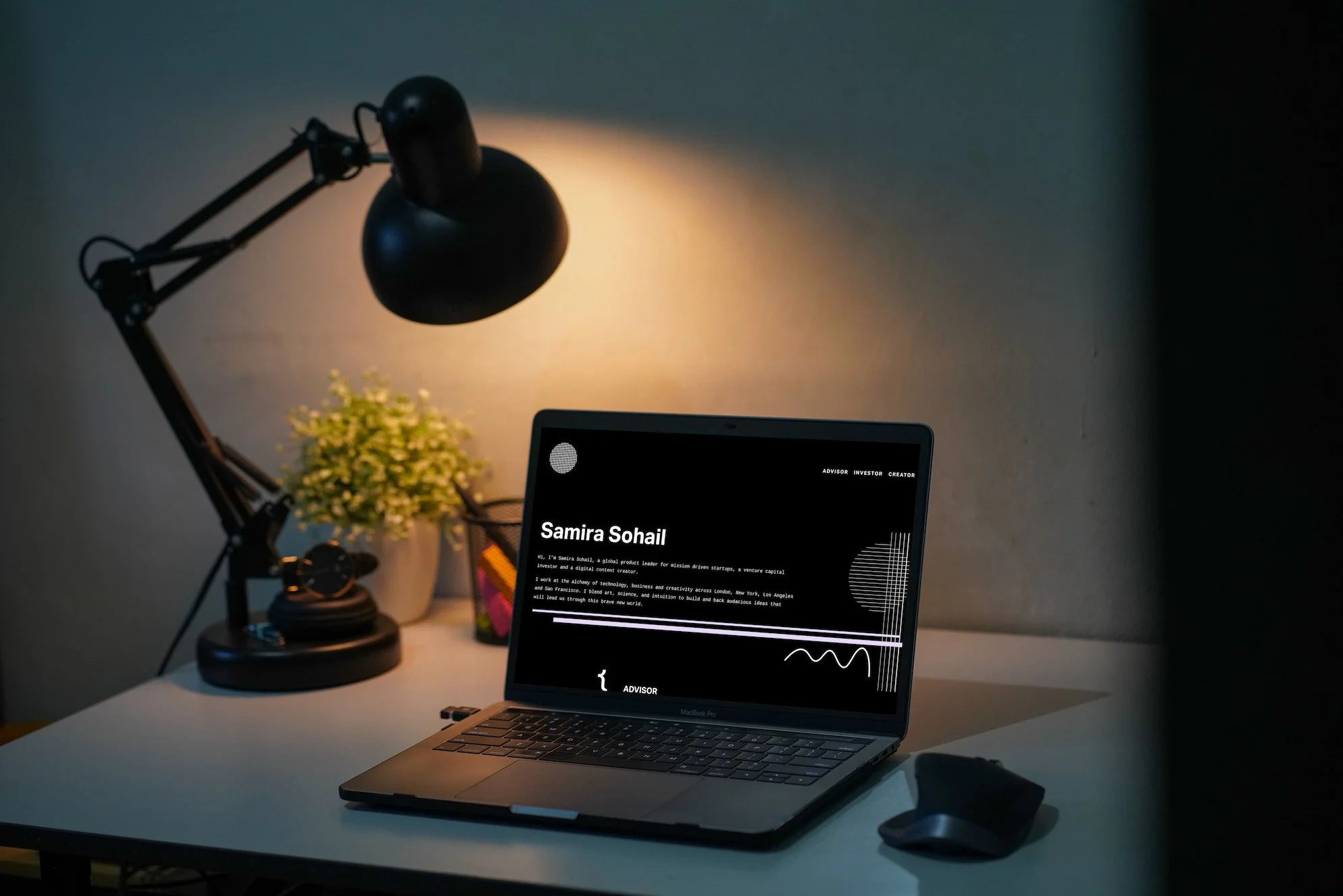 A workspace with a laptop displaying Samira Sohail's personal website, a black desk lamp illuminating the area, a potted plant, a headset, and a computer mouse on a white desk.