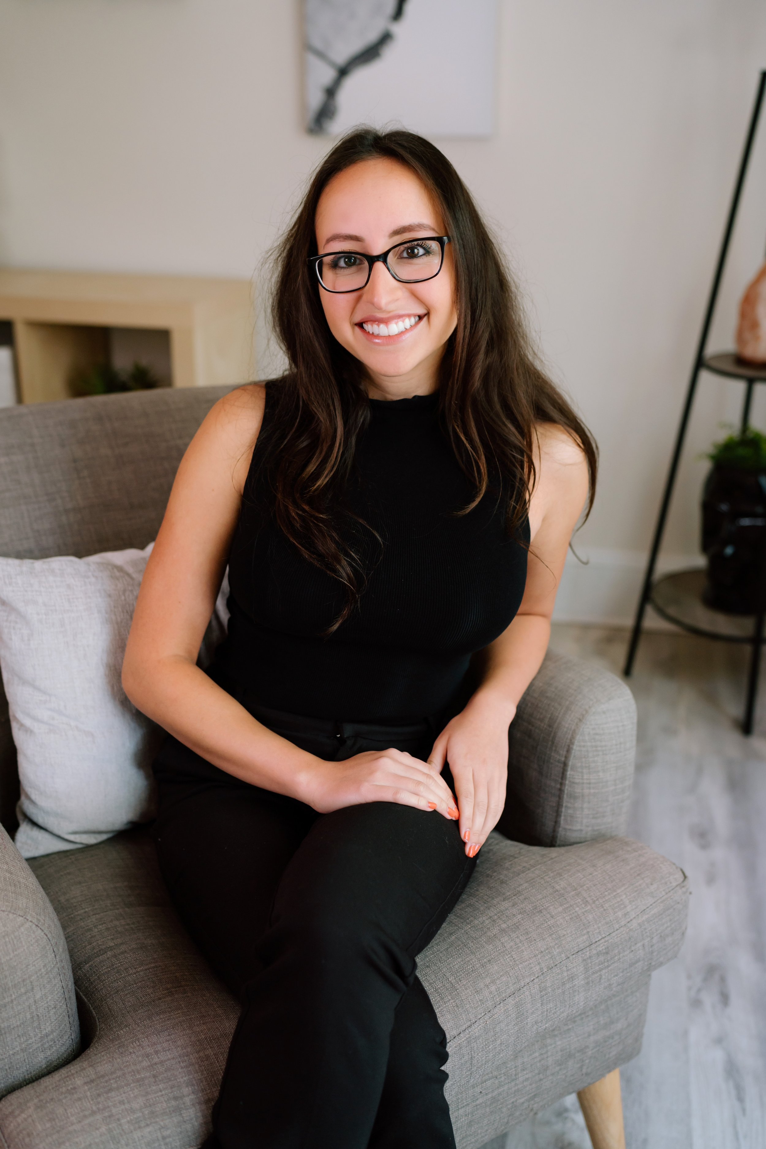 Woman with glasses smiling seated on a gray chair