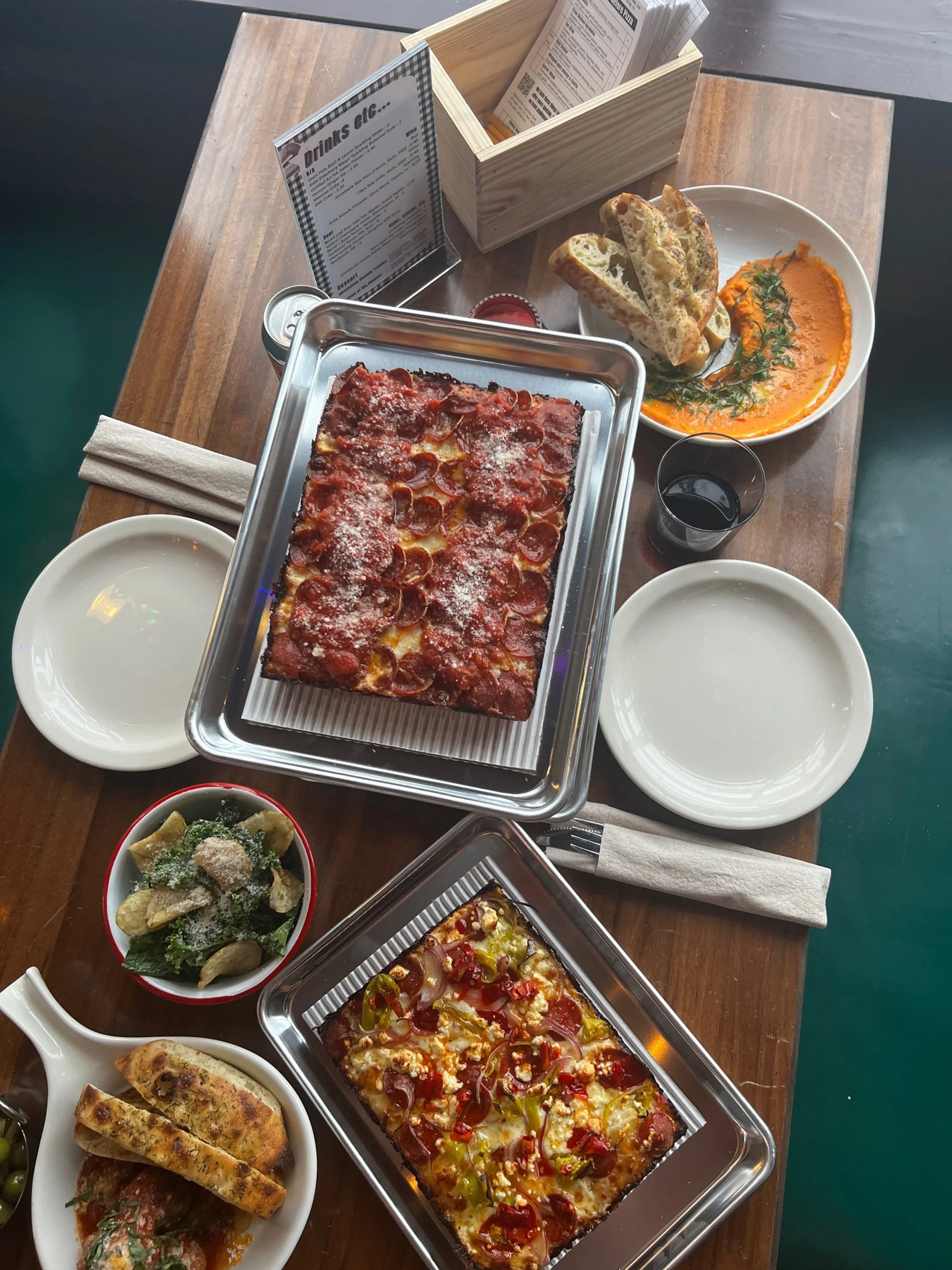 Pizza, bread, salad, and drinks on a wooden table at a restaurant.