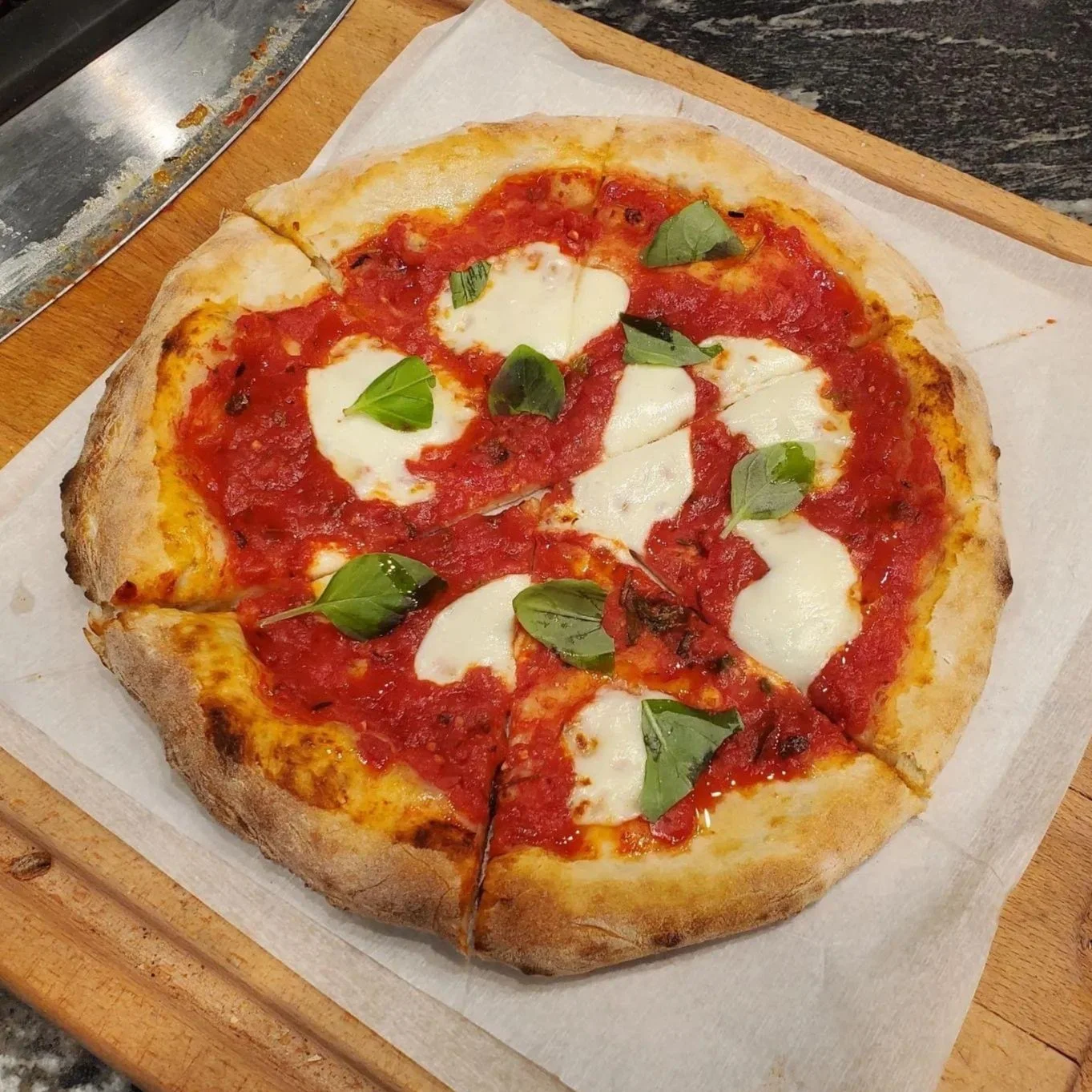Fresh Margherita pizza on a wooden board with tomato sauce, mozzarella cheese, and basil leaves.
