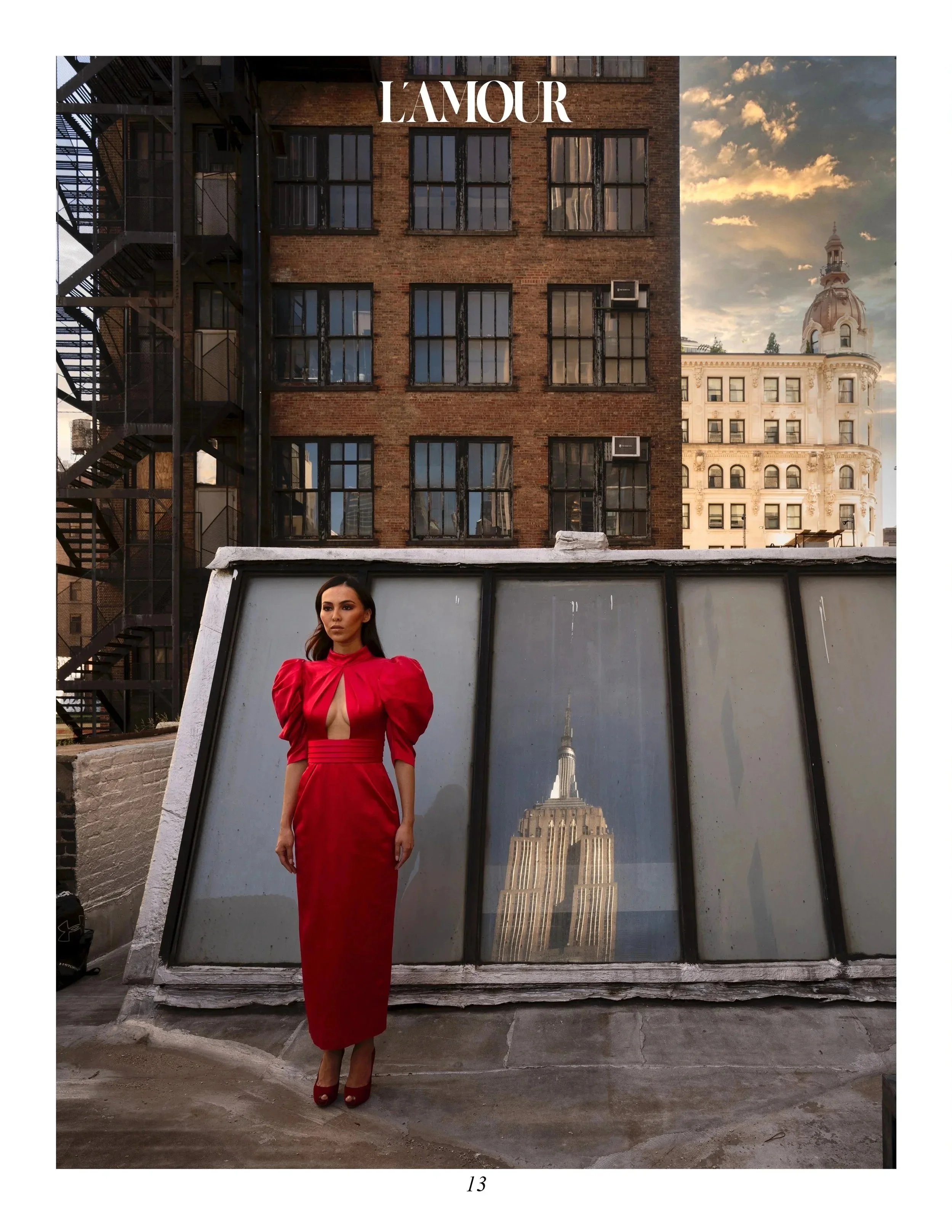 Woman in red dress standing on rooftop with city buildings and Empire State Building reflection.