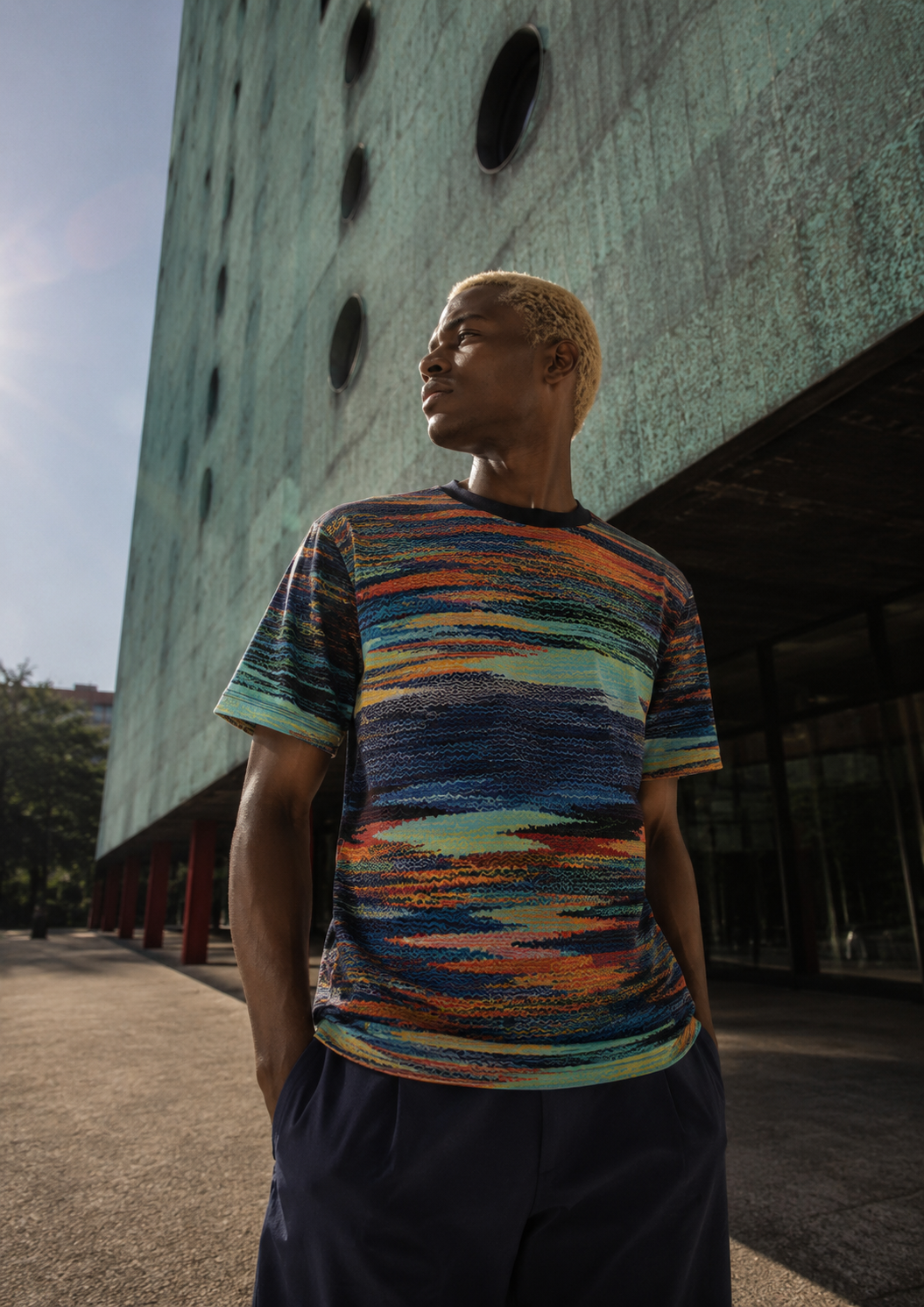 AI-created menswear campaign image for THE OUTNET by Alessia Moccia in São Paulo, featuring a man in a multicolored shirt against modernist architecture.