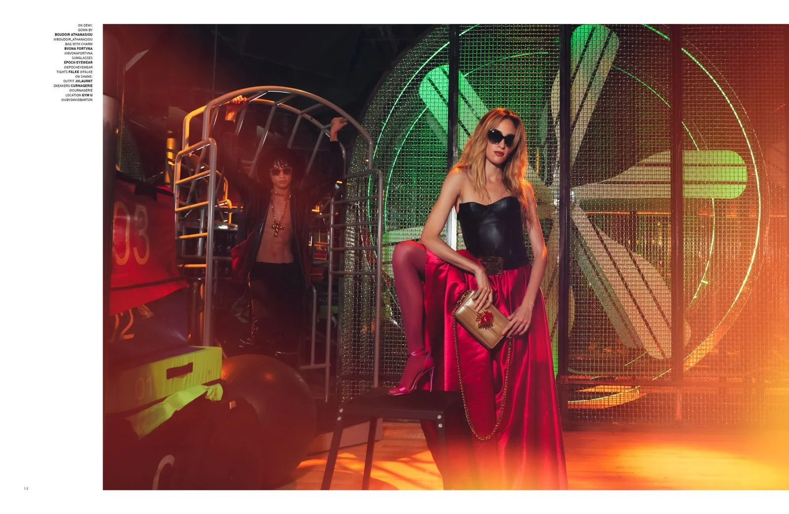 Fashion photoshoot with two models posing in a vibrant, industrial-themed setting, featuring colorful lighting.