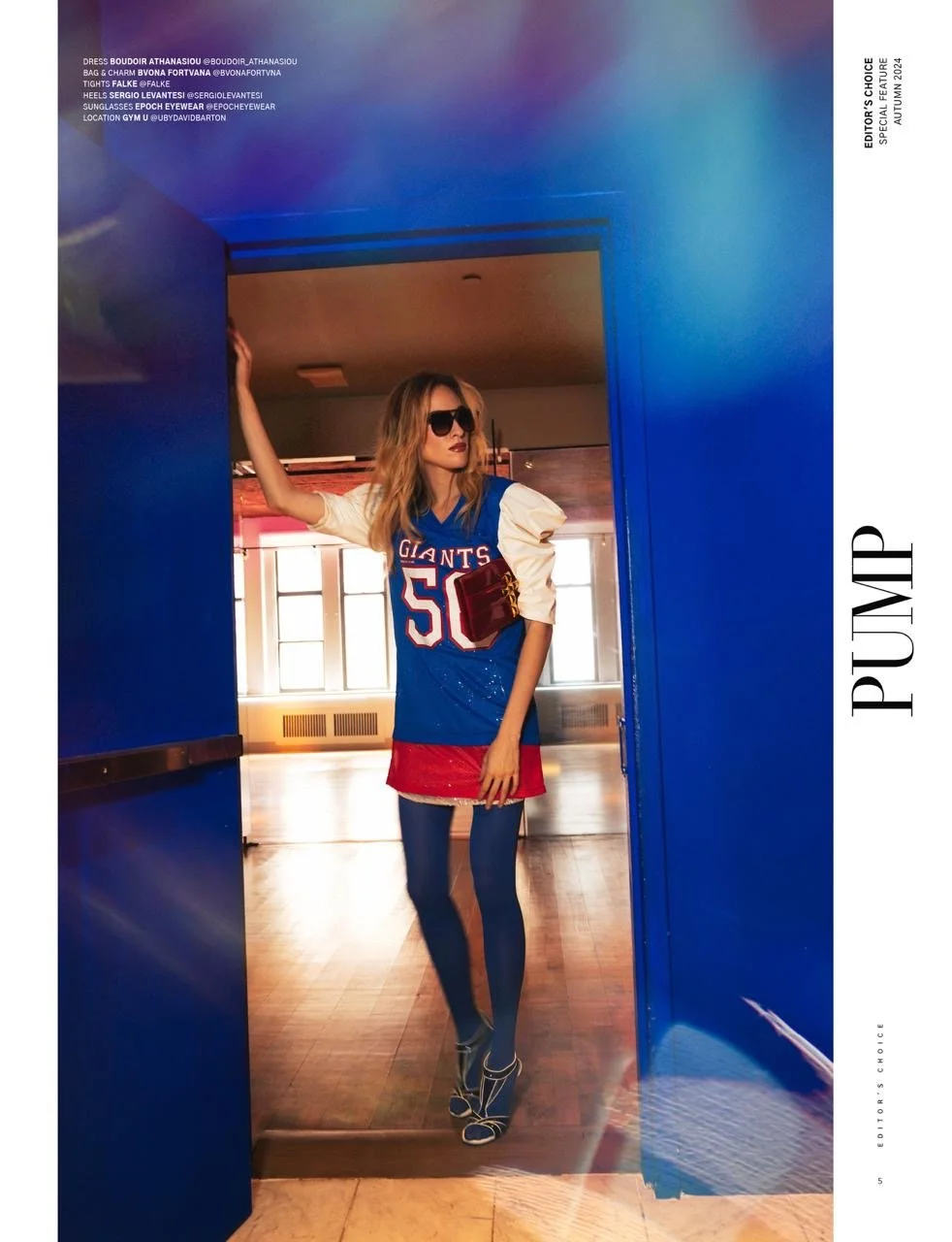 Fashion model in sports-themed outfit with sunglasses, standing in a blue doorway, featuring a "Giants" jersey-dress, tights, and high heels.