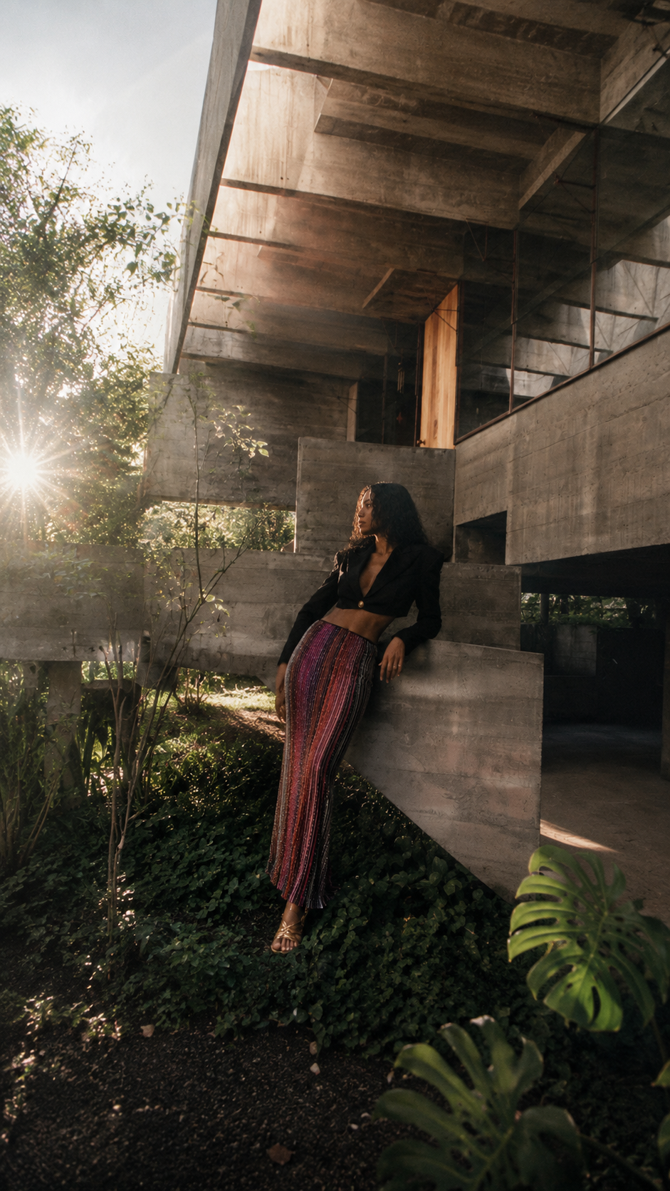 AI-directed fashion image for THE OUTNET by Alessia Moccia in São Paulo, featuring a woman in a shimmering skirt within tropical modernist architecture.