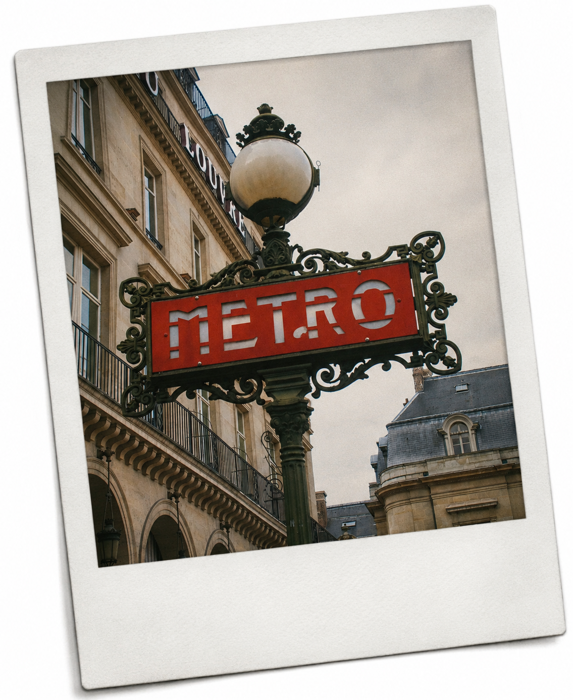 Paris Metro sign with ornate black ironwork and a round street lamp on a cloudy day