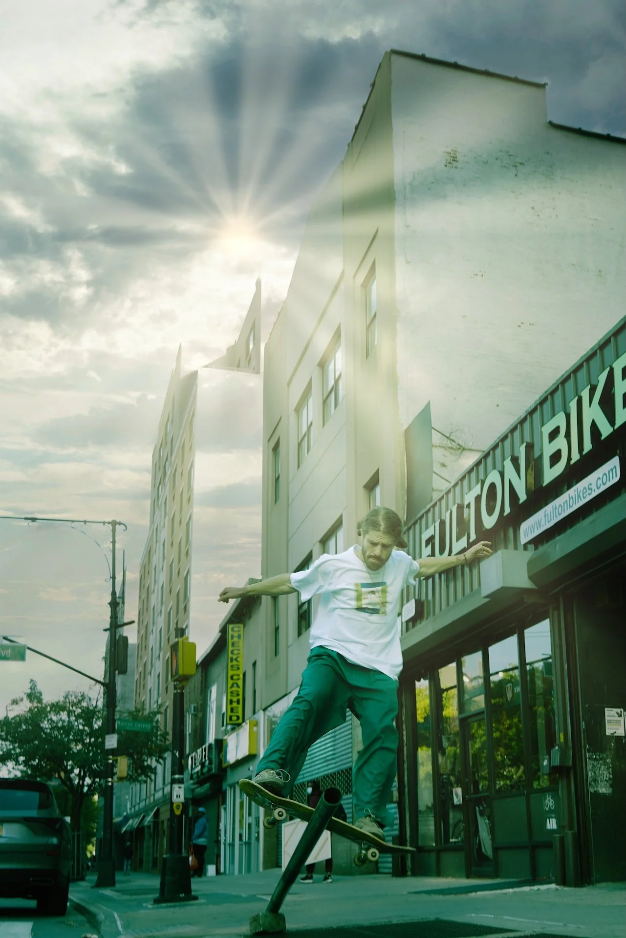A man skateboarding on a handrail in an urban area with buildings, traffic lights, and a cloudy sky with sunlight.