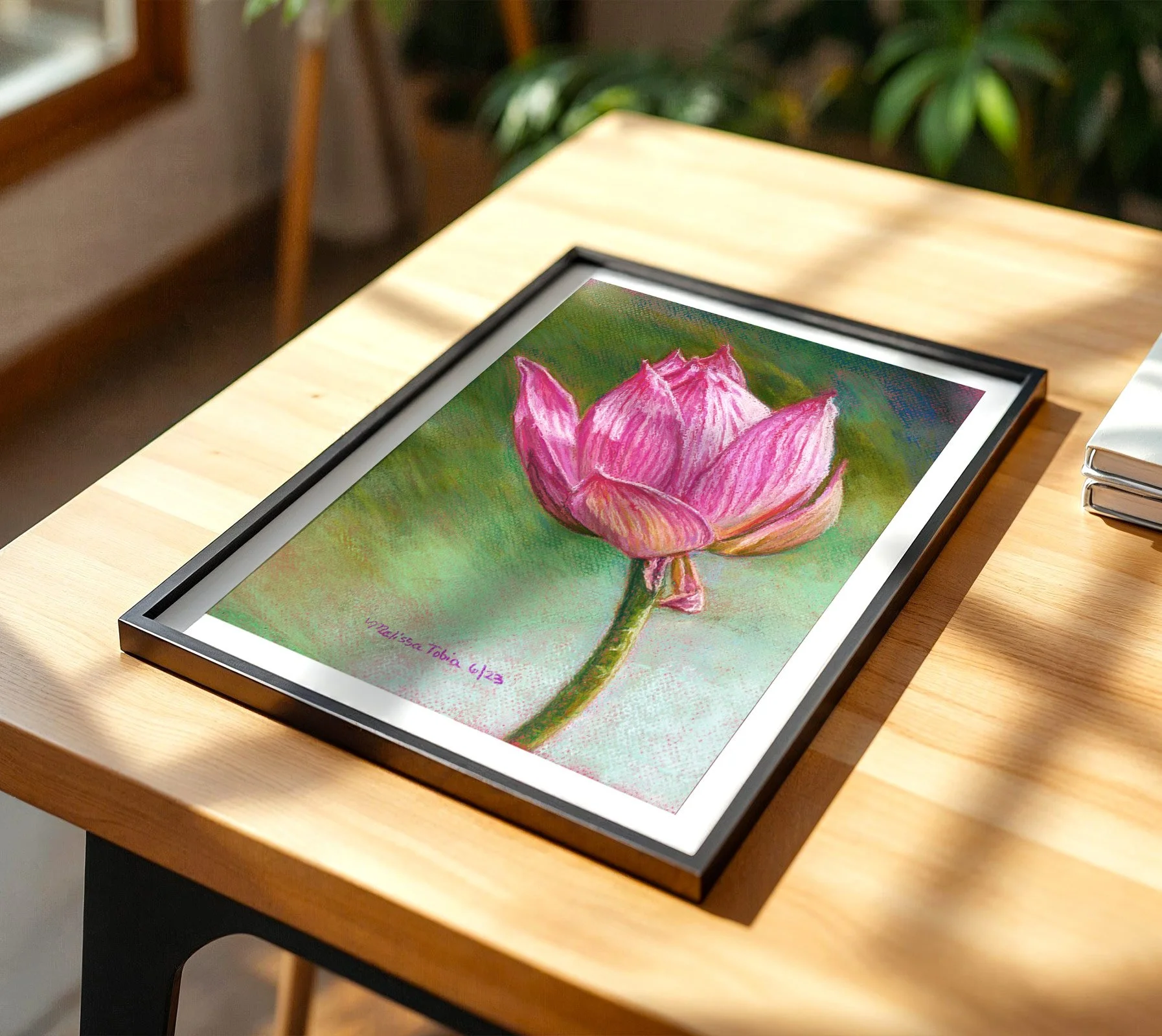 Framed pink lotus painting print resting on a wooden table