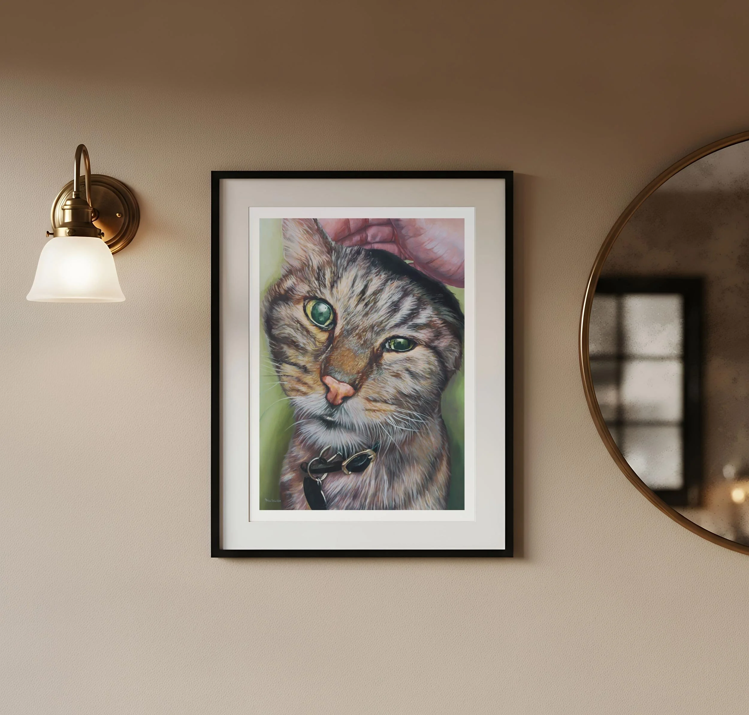 Tabby cat art print framed and hung on a wall beside a wall sconce and round mirror