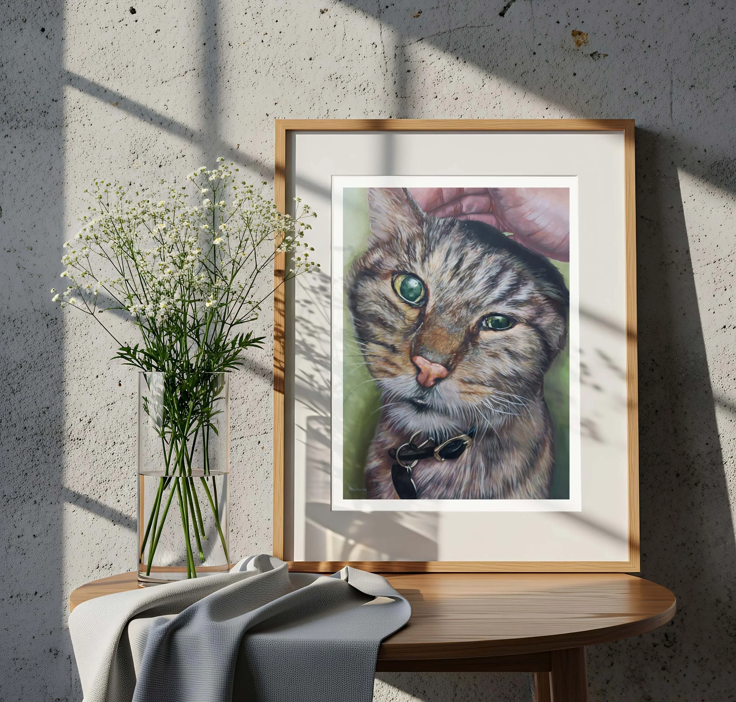 Tabby cat portrait print on a side table near fresh flowers and a draped cloth