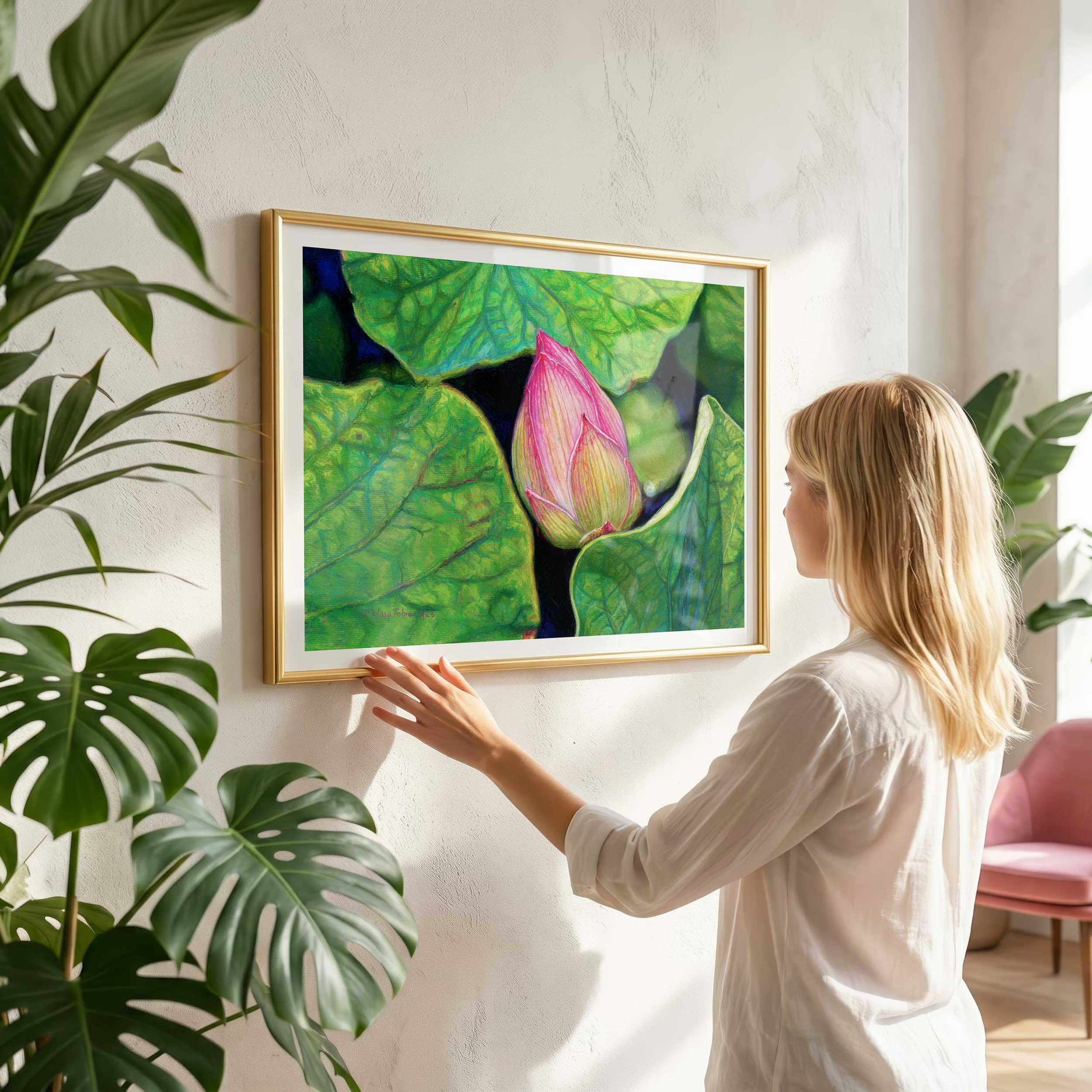 Woman hanging a large framed pink lotus pastel print on a wall, showing scale