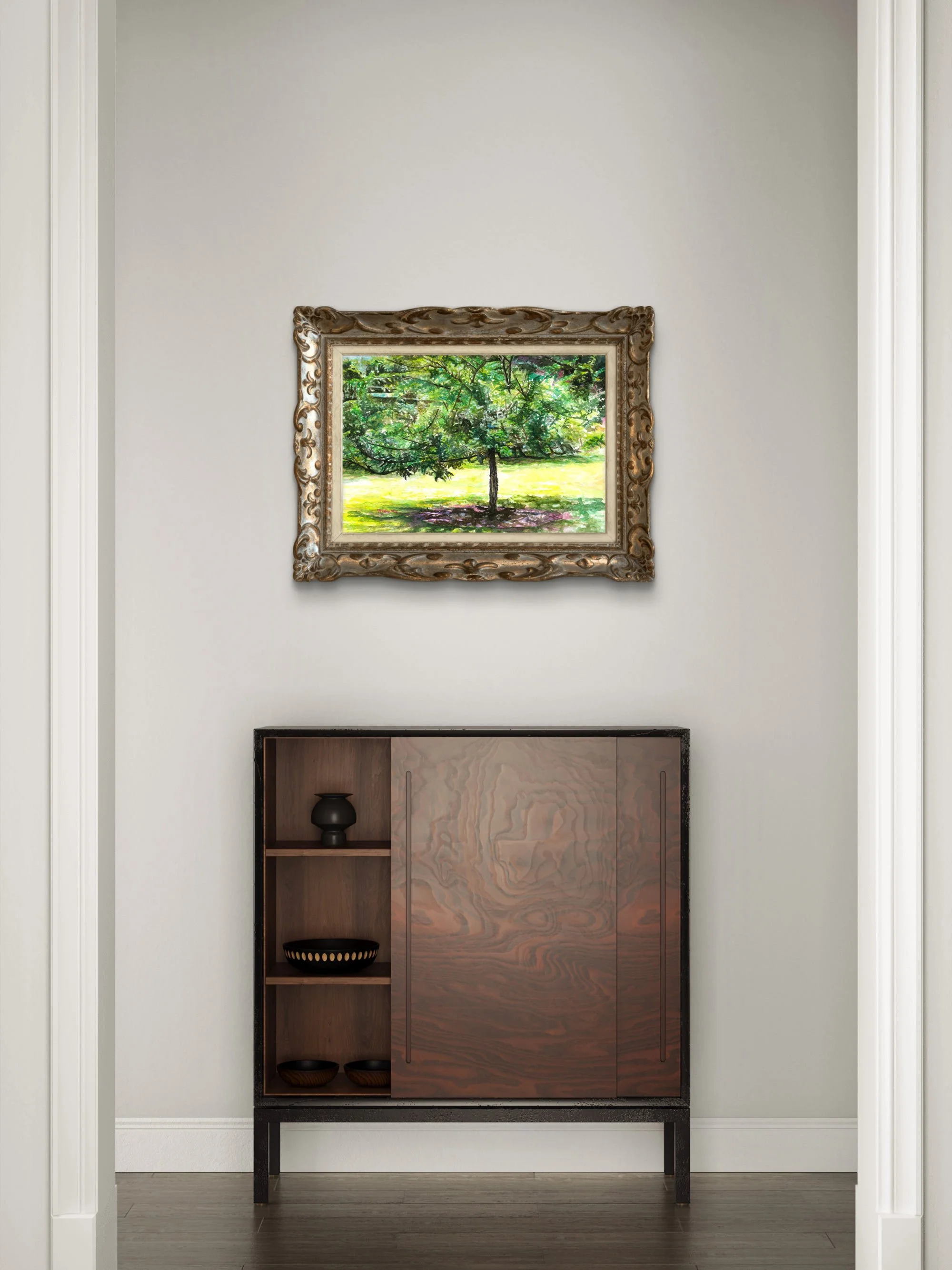 Framed tree watercolor in a gold frame on a white wall above a dark wood cabinet