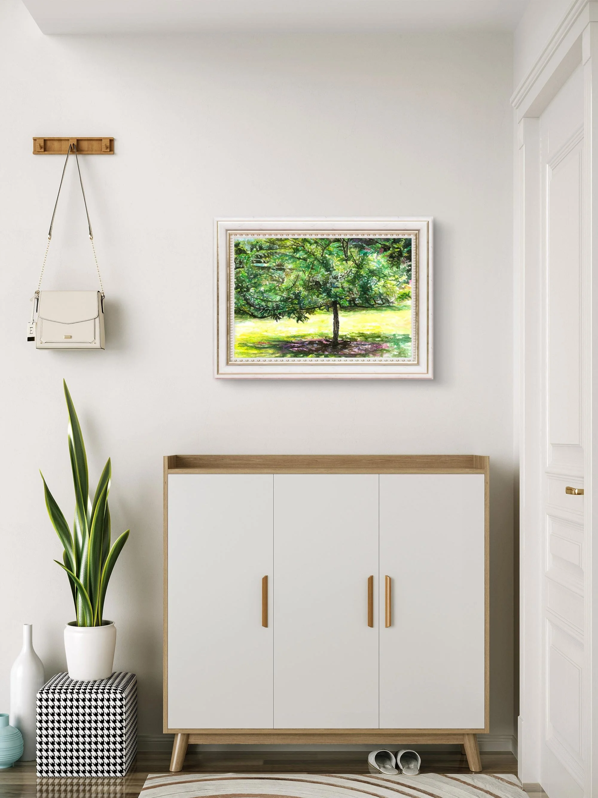 Framed tree watercolor on a white wall above a cabinet with a hanging bag and snake plant
