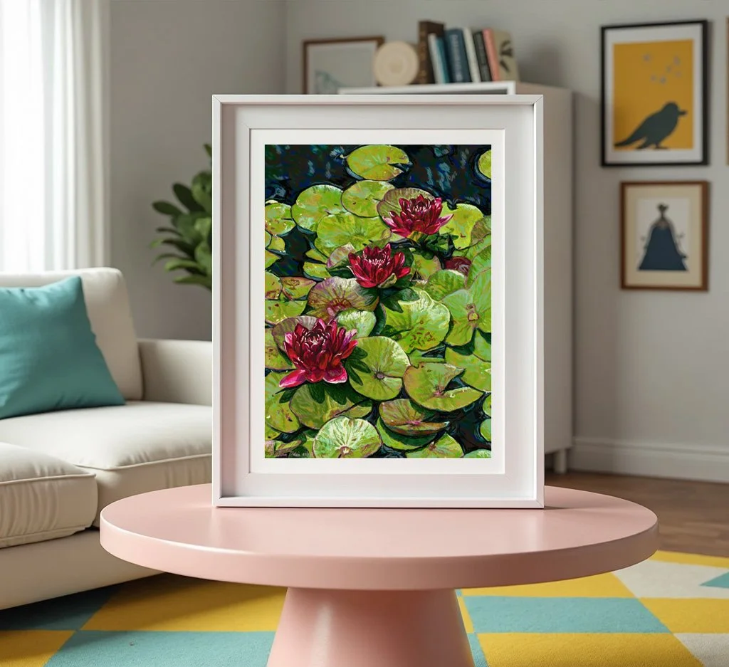 Water lily wall art in a white frame on a pink round table in a living room with a sofa and bookshelf