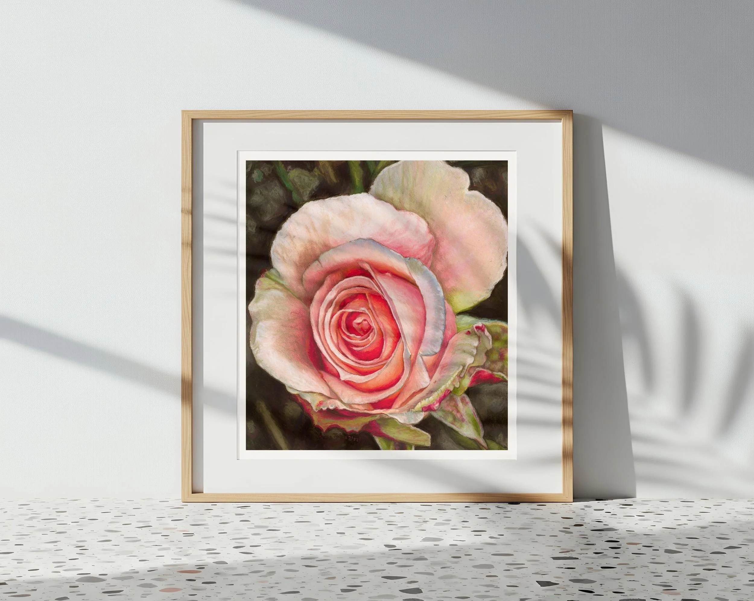 Framed rose art print leaning against a terrazzo tile floor