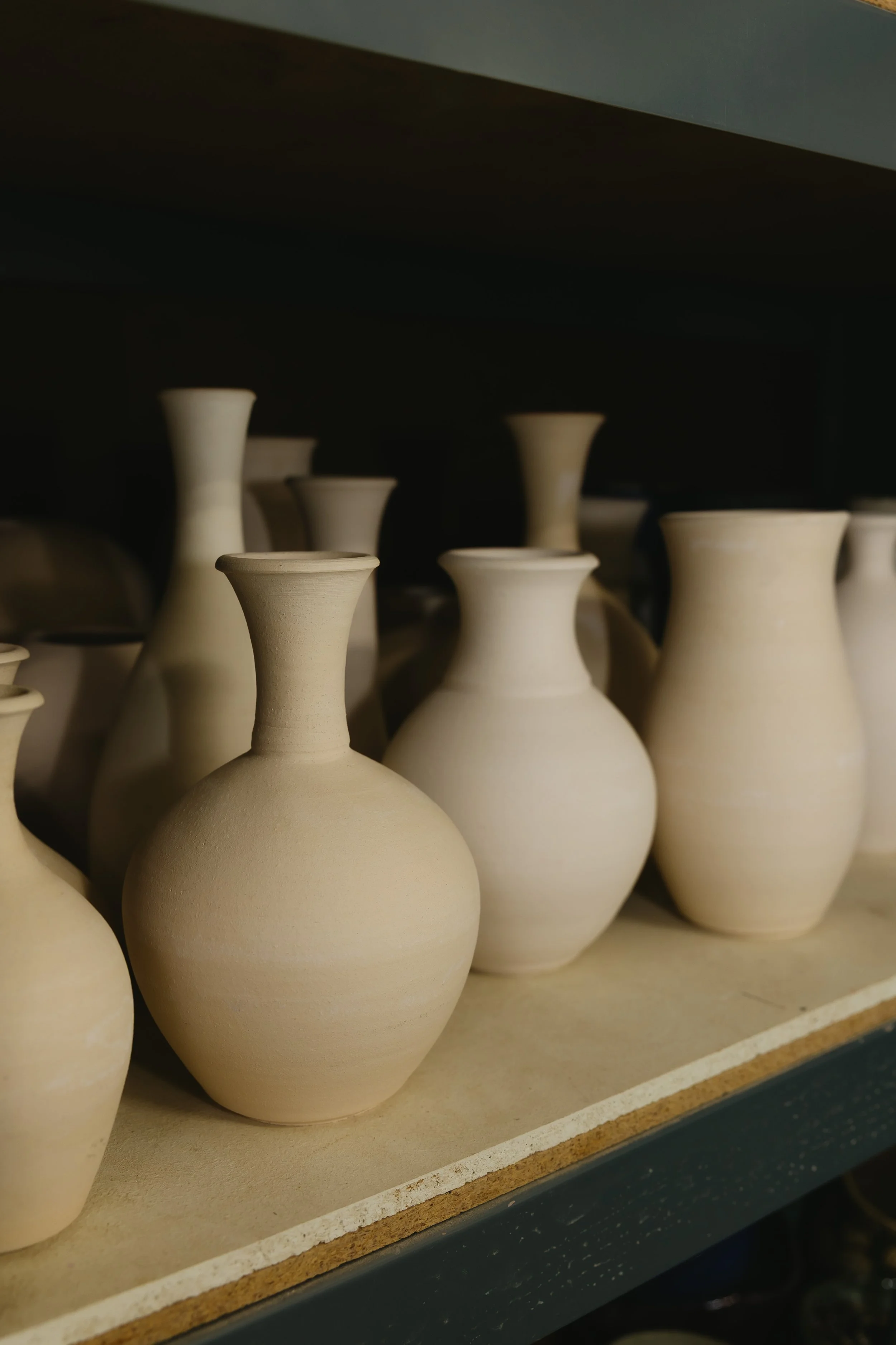 Multiple unfinished ceramic vases on a shelf in a pottery studio.