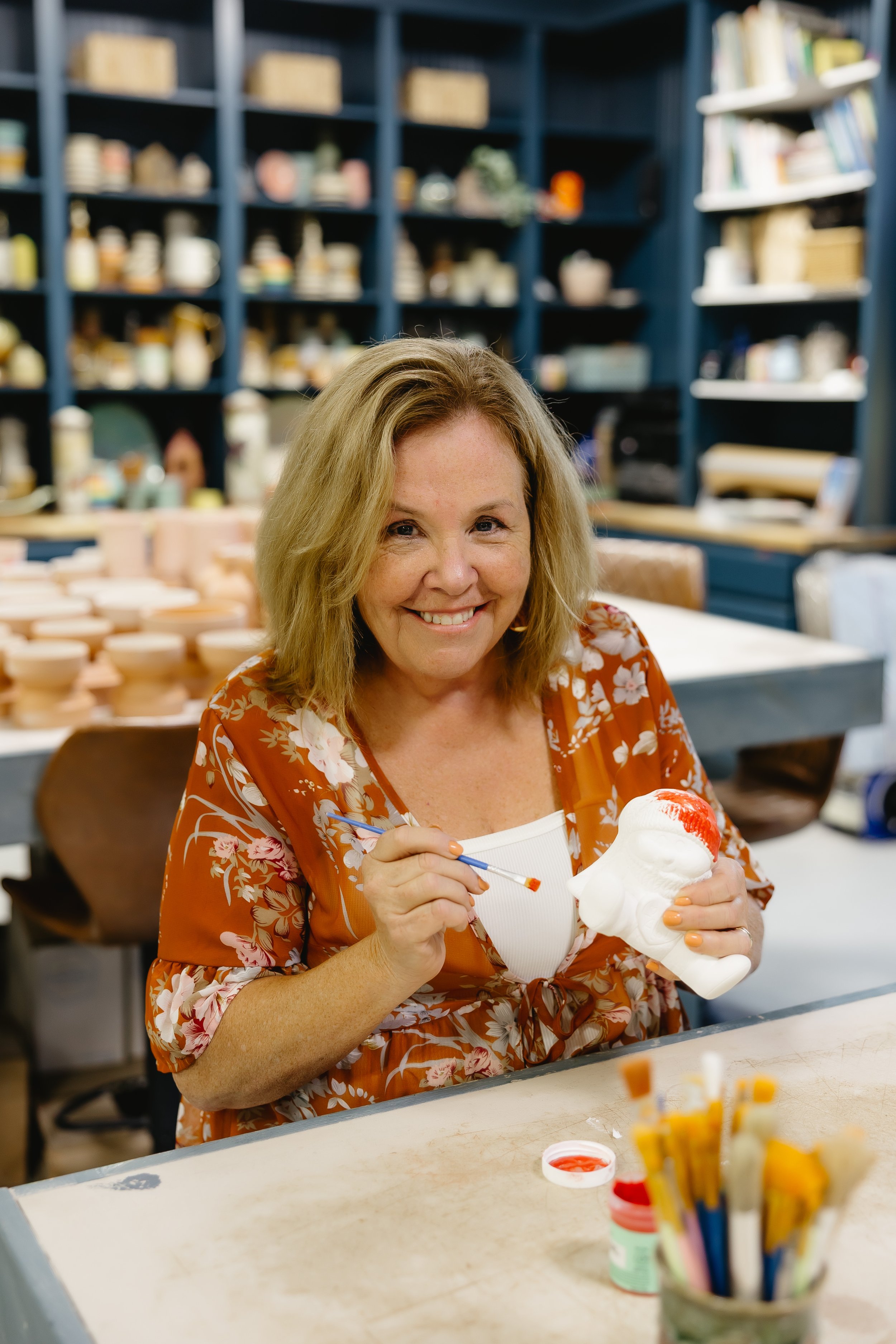 Woman painting a small ceramic sculpture in an art studio or ceramics workshop.