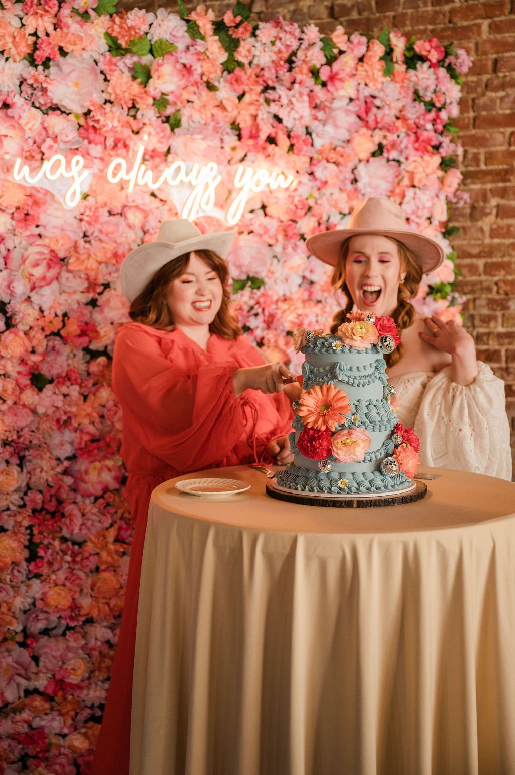 couple cutting blue cake in front of pink flower wall
