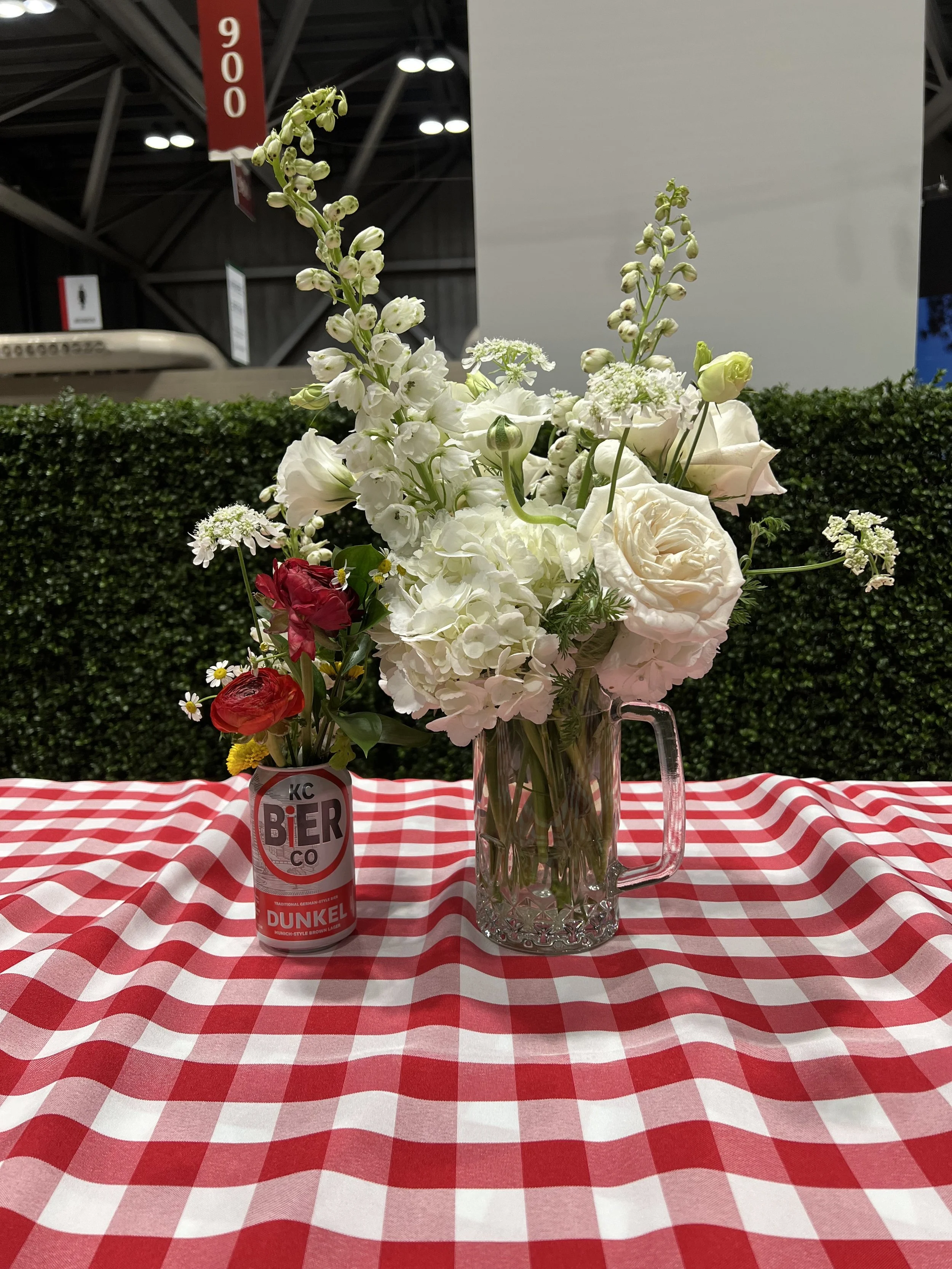 kc bier co can and glass beer stein used as vases with white and red florals on gingham table cloth