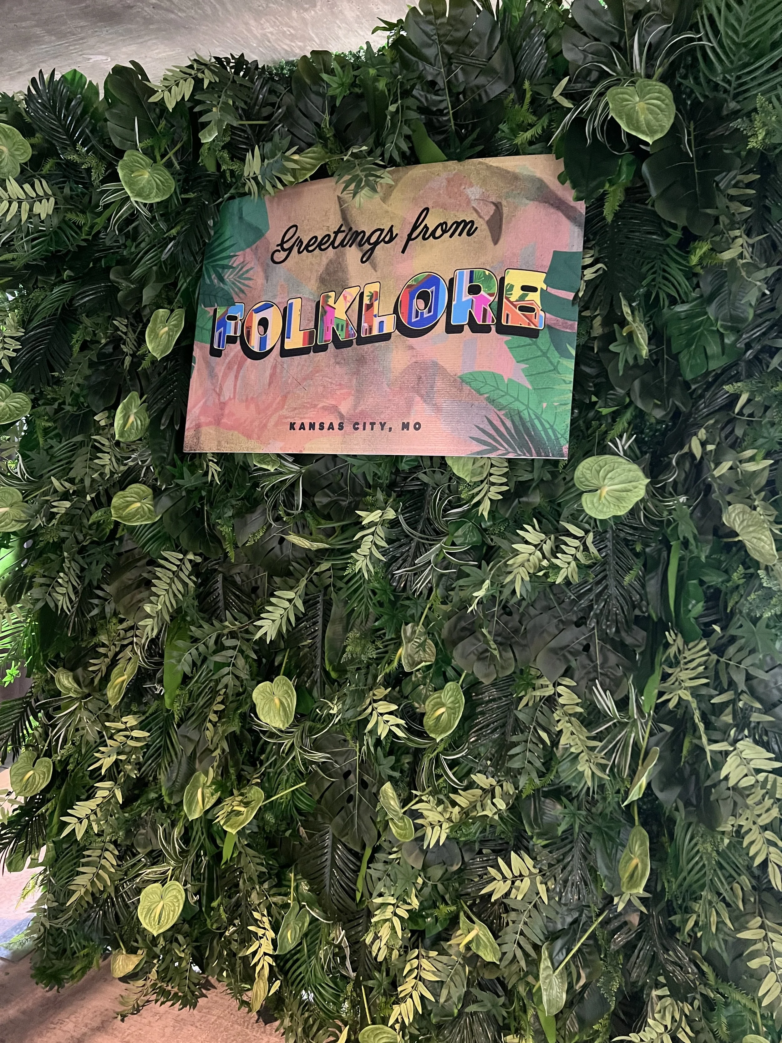tropical greenery wall with event sign that says folklore