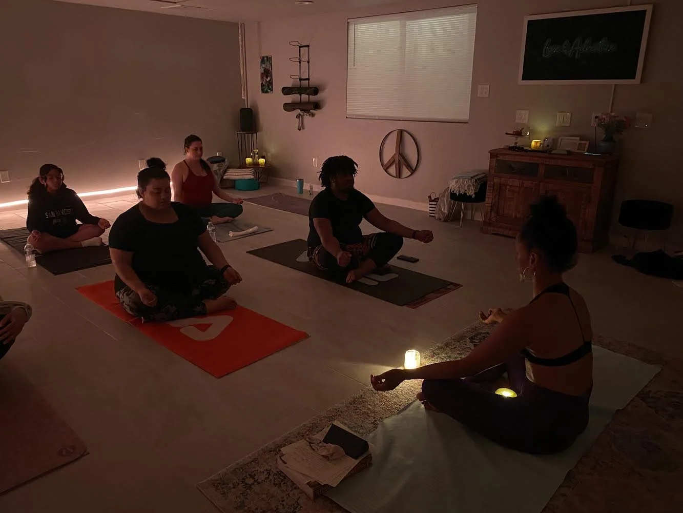 Group meditation class in dimly lit room with yoga mats and candles