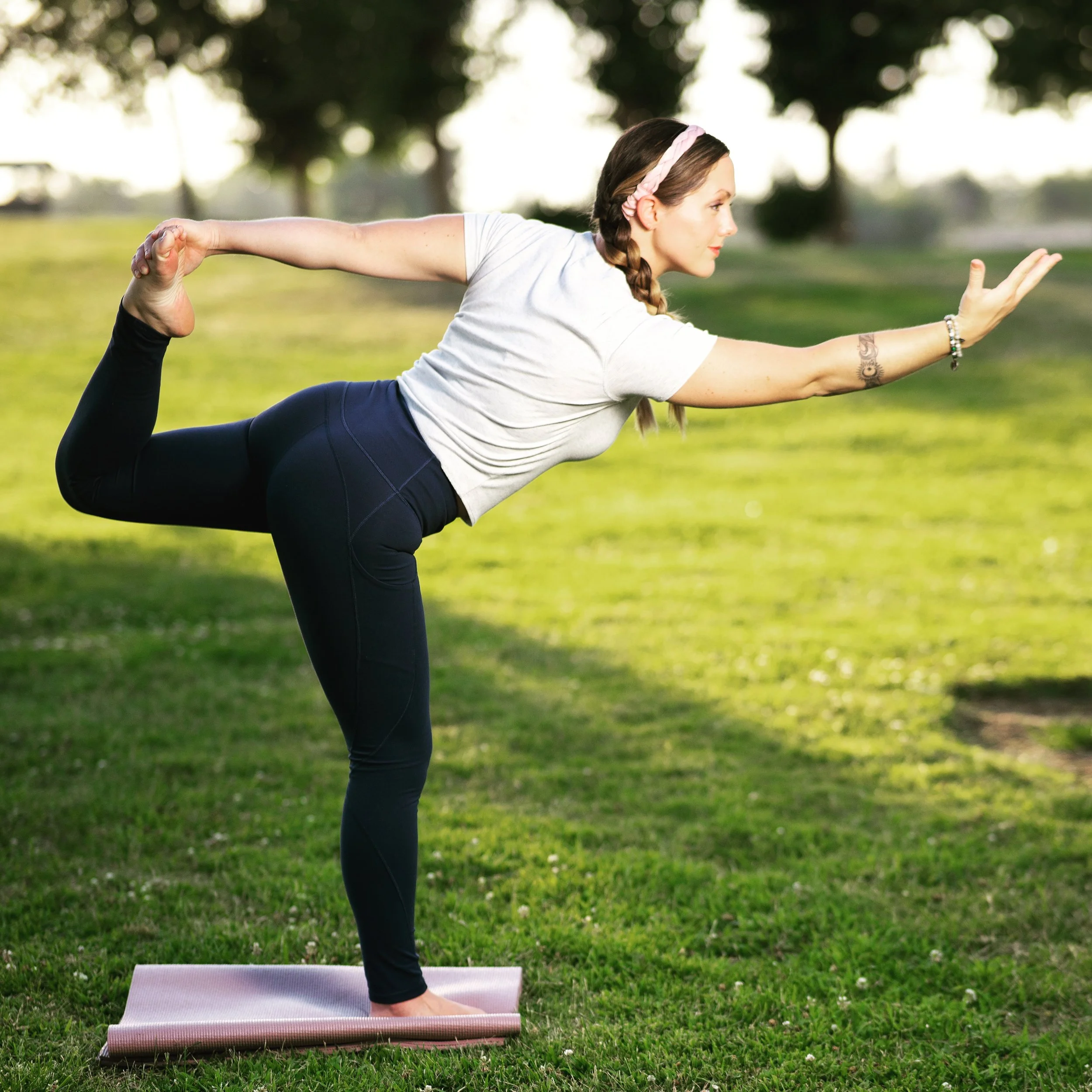 Woman practicing yoga in Dancer Pose outside on a grass field.