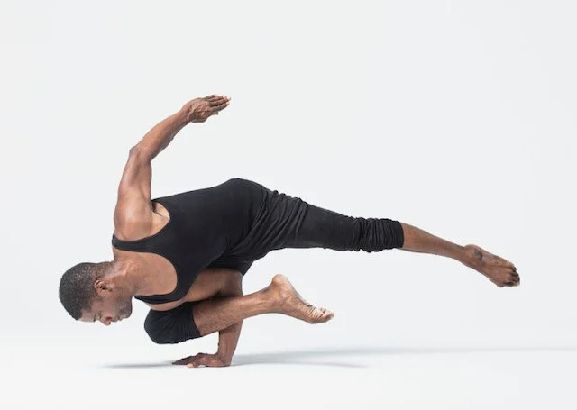 A person performing a one-handed yoga pose balancing on one arm with their legs extended.