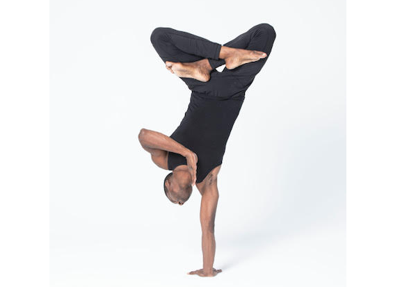 A person performing a one-handed handstand with their legs crossed in a yoga pose on a white background.