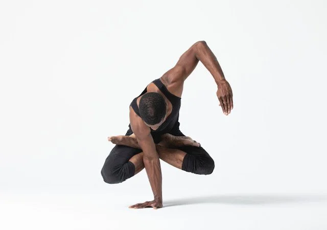 A man in black athletic wear performing a complex acrobatic balance pose against a plain white background.