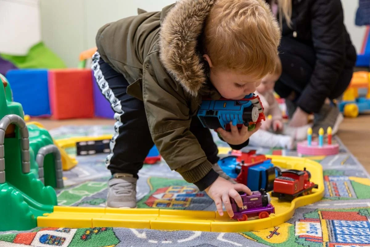 Child in a green parka playing with toy trains on the floor