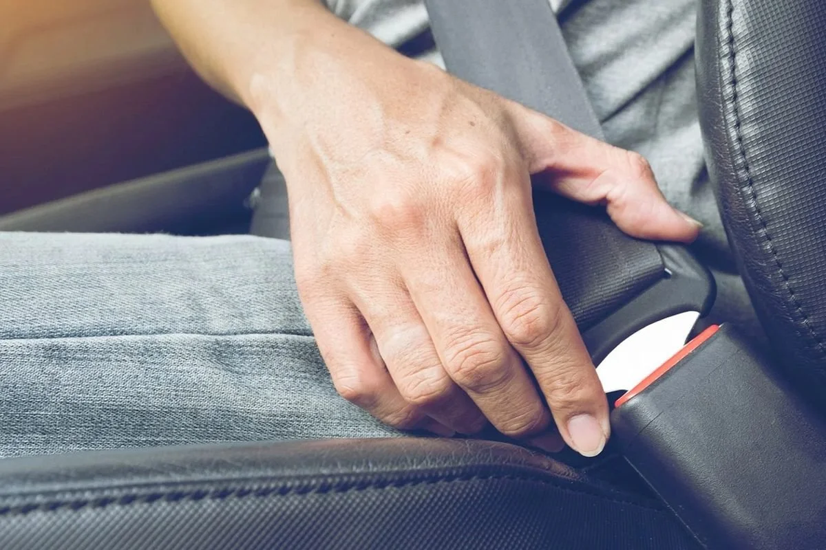 Hand reaching for a seat belt buckle beside a car seat