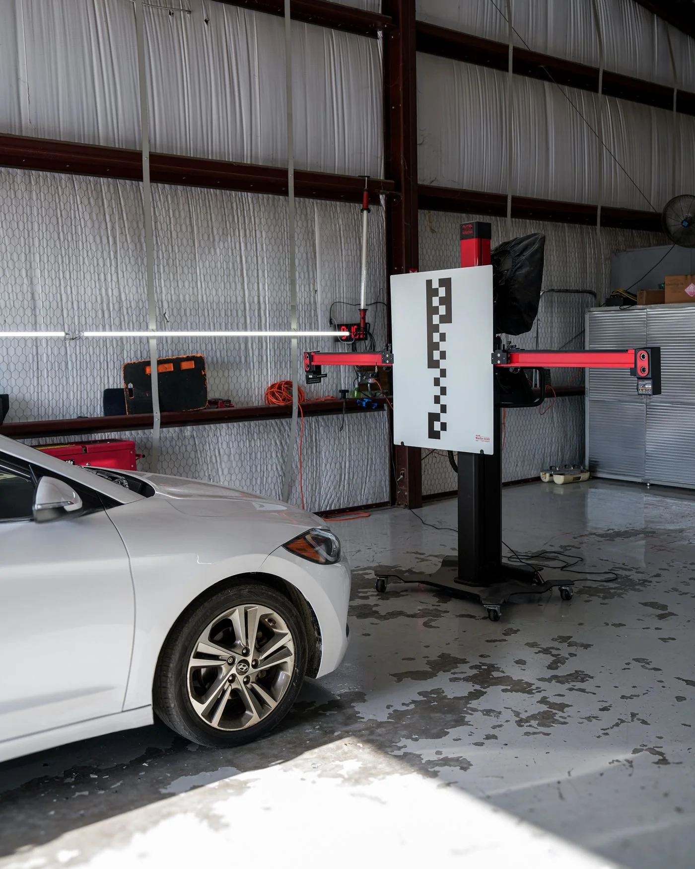 ADAS calibration frame with a target board set up in front of a white car in the DNA Safety Repair shop