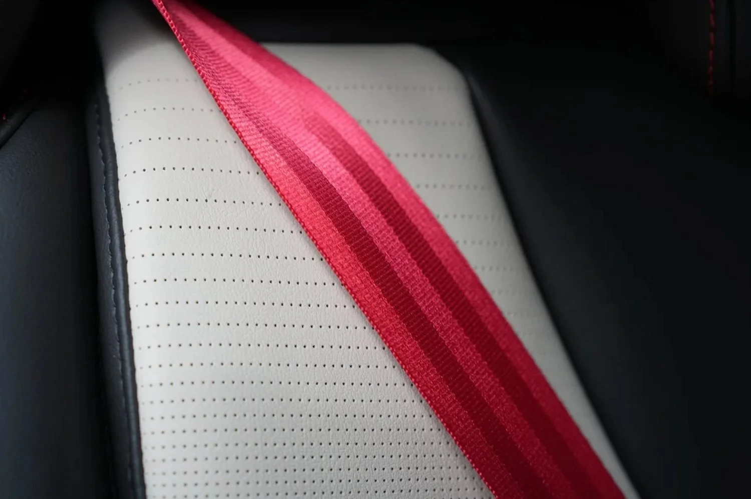 Red custom-color seat belt webbing across a light leather seat