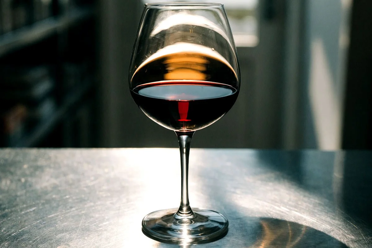 Red wine in a glass on a stainless steel counter.