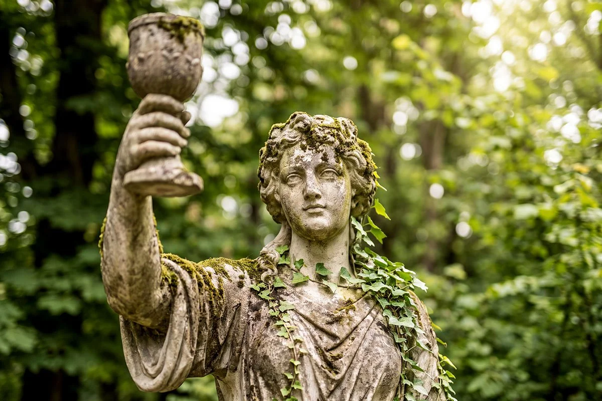 Front view of a statue in a French park holding a glass of wine.