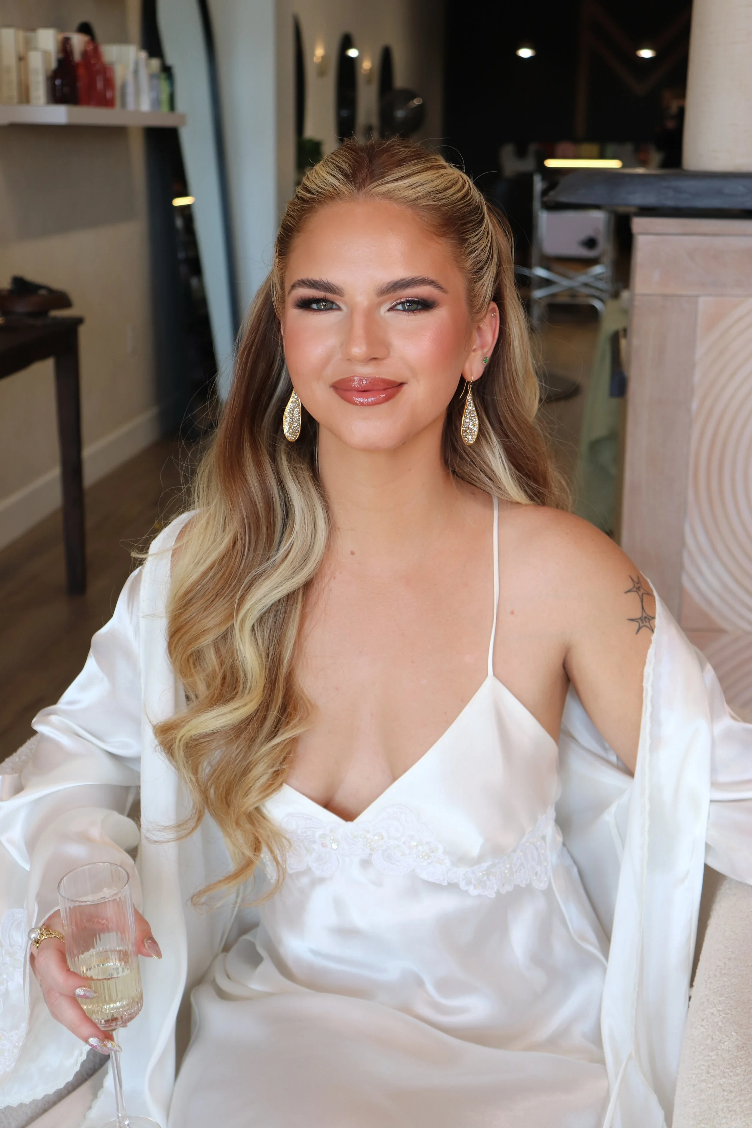 A woman in a white lace off-shoulder wedding dress, smiling, indoors with vintage decor and patterned carpet.