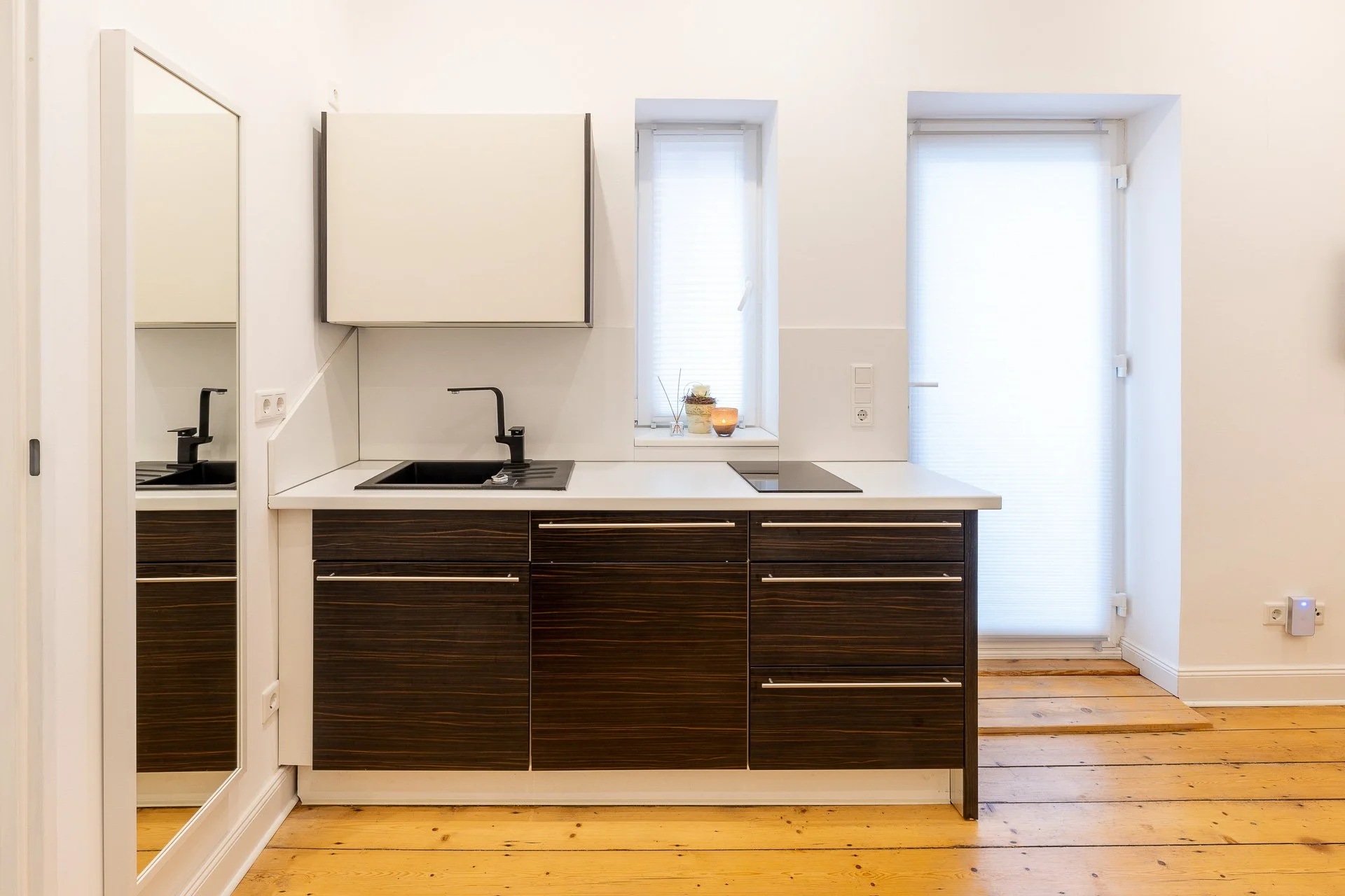 Moderne Küche mit dunklen Holzschränken, Waschbecken und Herd, Fenster mit Jalousien, helle Wände und Holzboden.