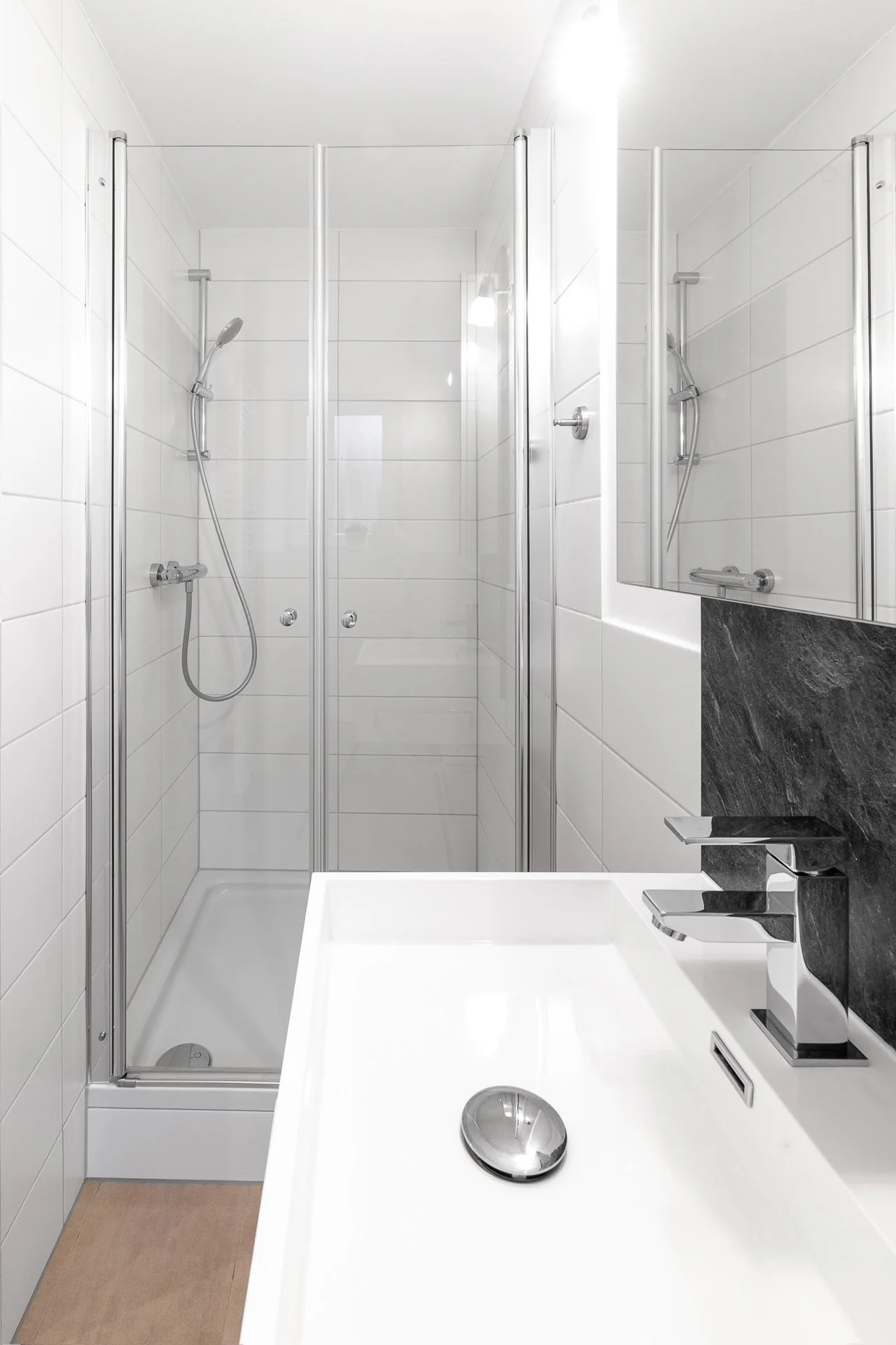 Moderner Badezimmerbereich mit Dusche und Waschbecken, weiße Fliesen, Glasduschtüren, stilvolle Armaturen, heller Raum.