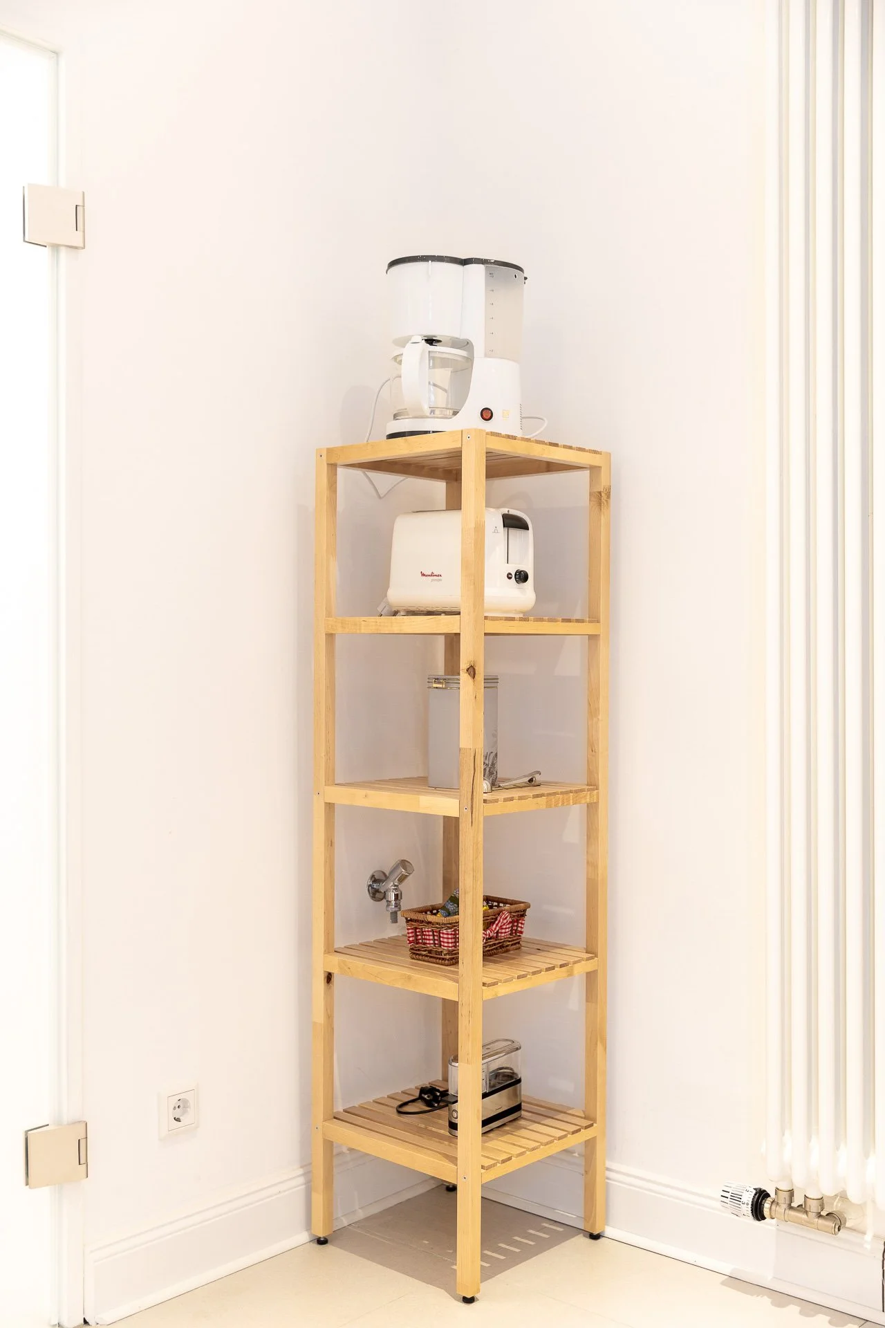 Holzregal in einer Ecke mit Küchenutensilien: Kaffeemaschine, Toaster, Korb und Mixer.