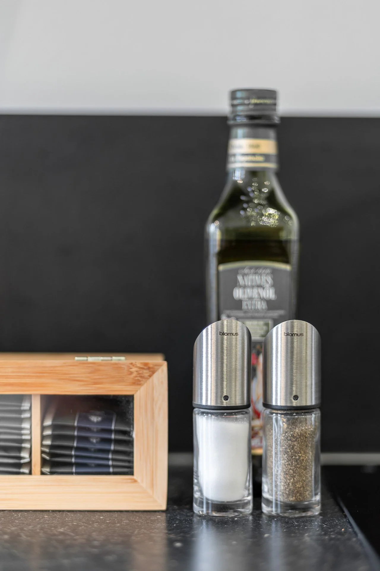 Ölflasche und Gewürzstreuer auf einem Küchentisch, neben einer Teebox aus Holz.
