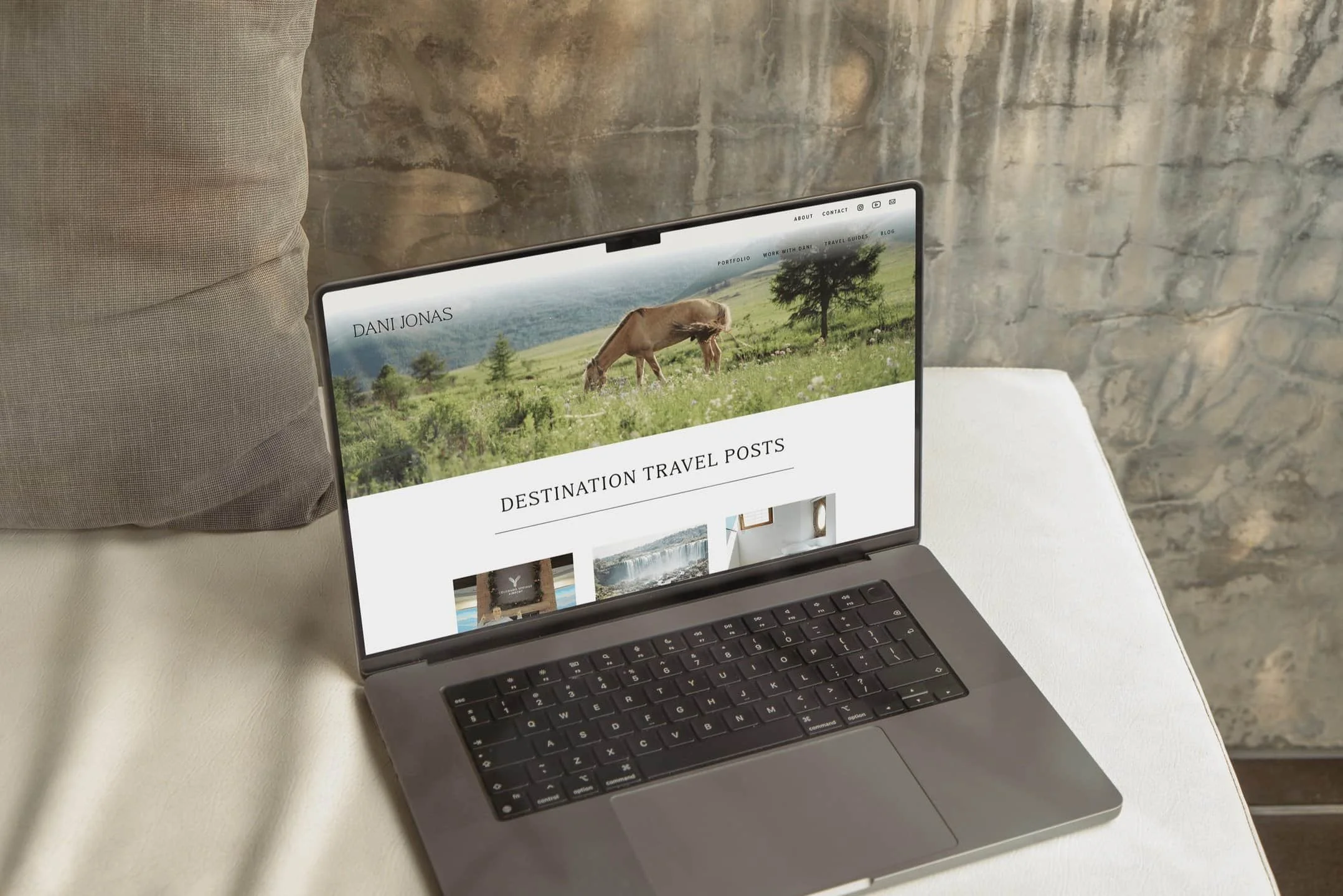 A laptop on a white surface displays a blog about destination travel posts, featuring a photo of a grazing horse.