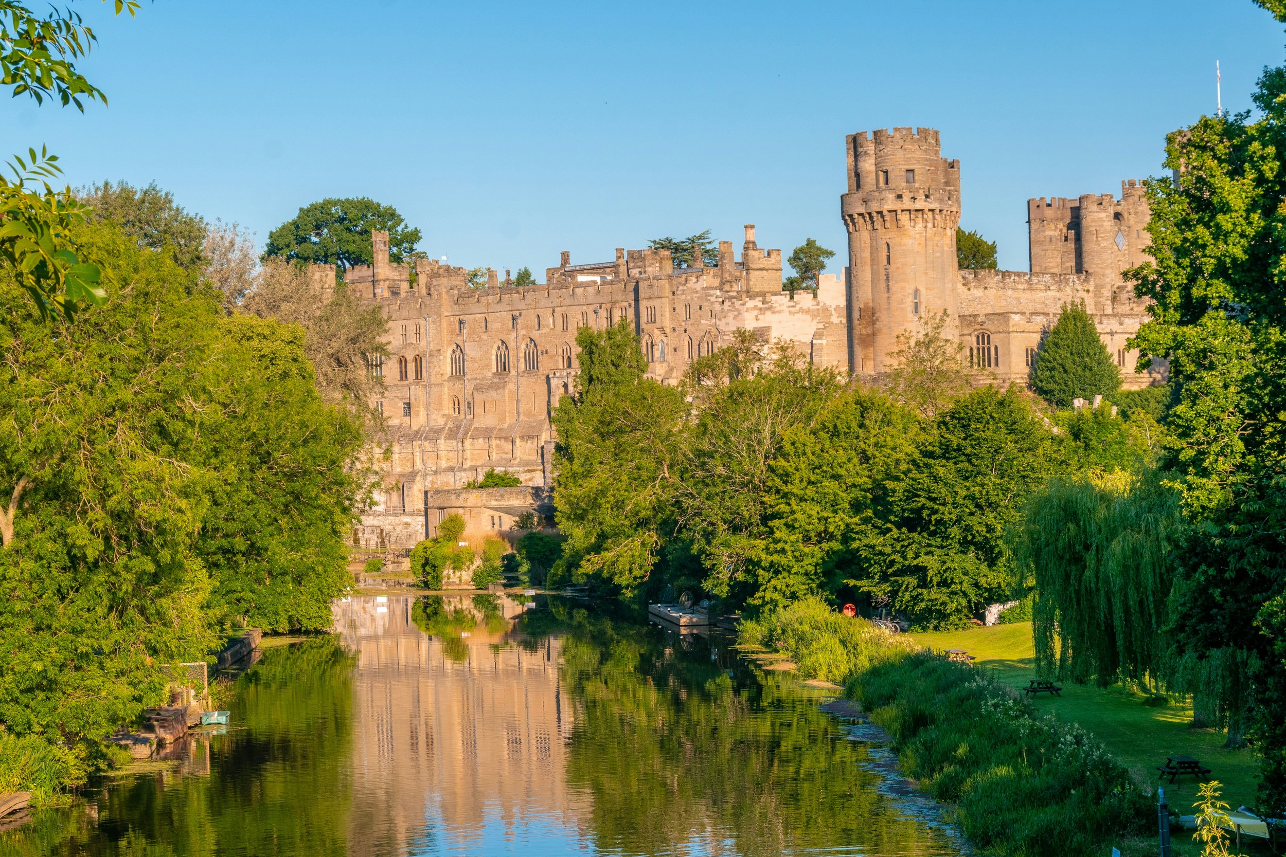 Aerial view of Warwick Castle in England with stone towers, large windows, and visitors walking across the green lawn in the inner courtyard.