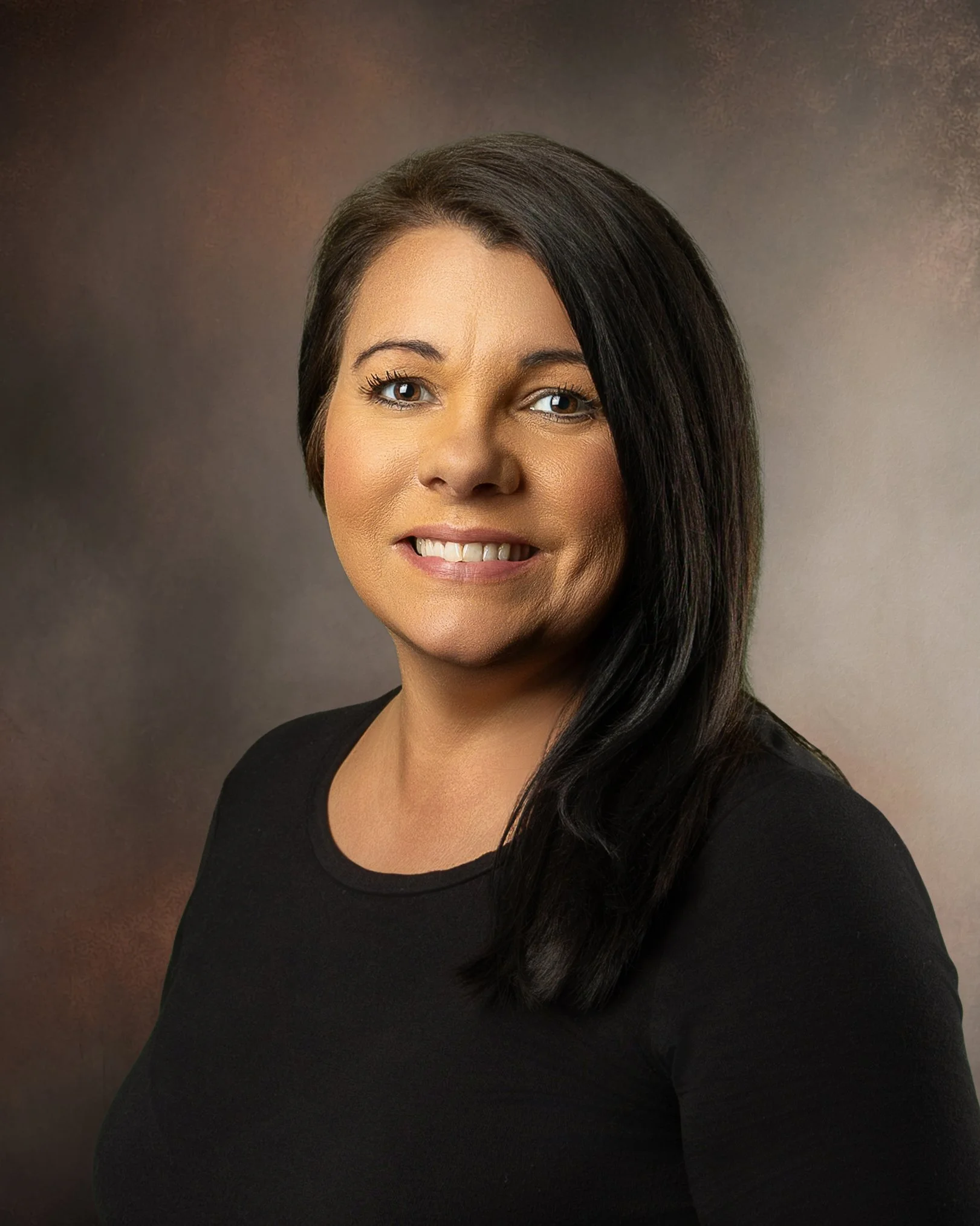 Headshot of a woman with long dark hair, wearing a black top, smiling against a brown textured background.