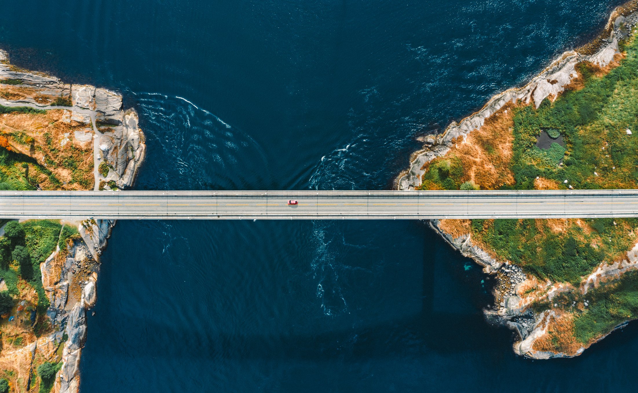 Luchtfoto van een brug over een rivier met omliggende groene en roestkleurige rotsachtige gebieden.
