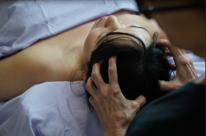 Person lying down with eyes closed, receiving a head massage from  Anne Heckheimer (our founder).