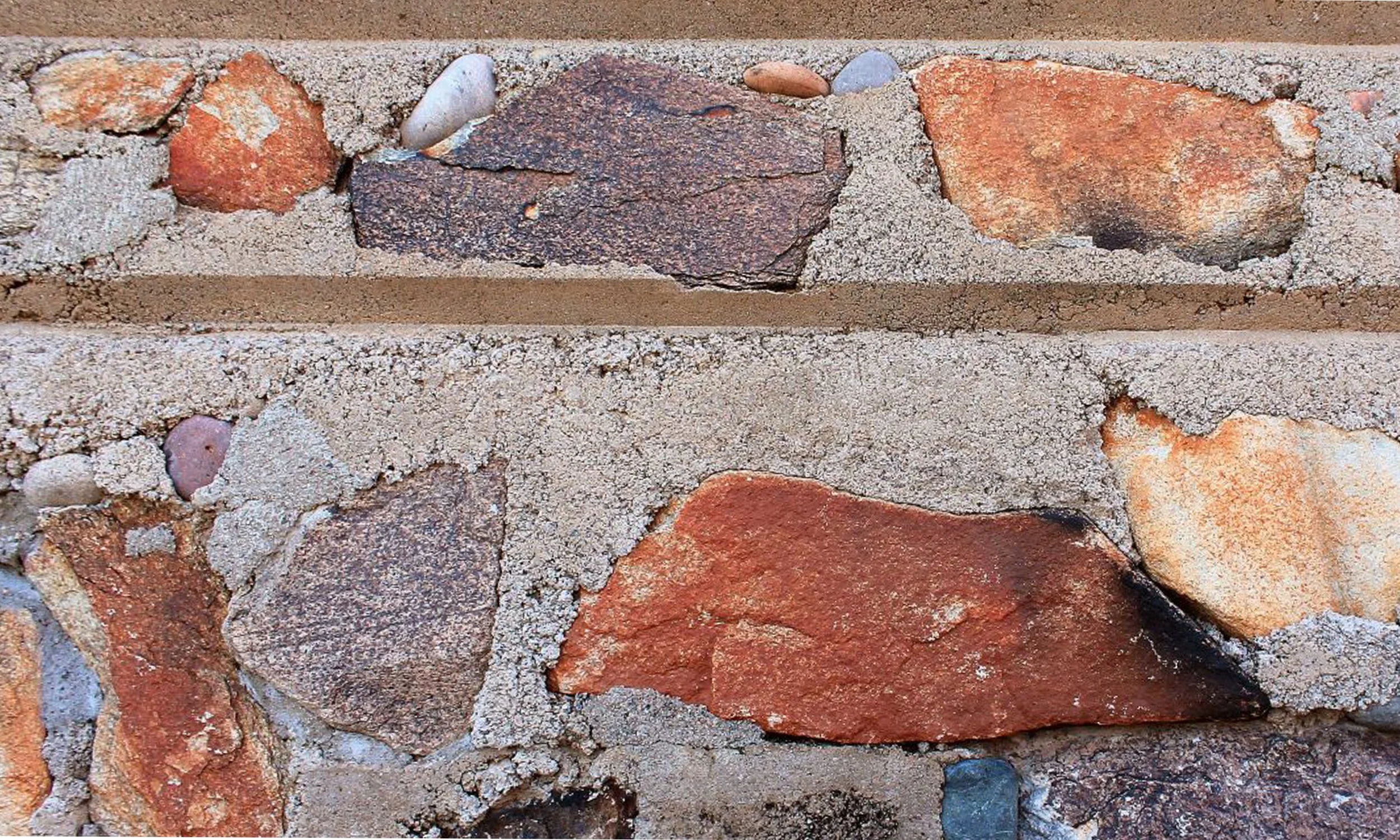 Close-up of a brick wall showing red and brown bricks with light gray mortar and some small pebbles embedded in the mortar.